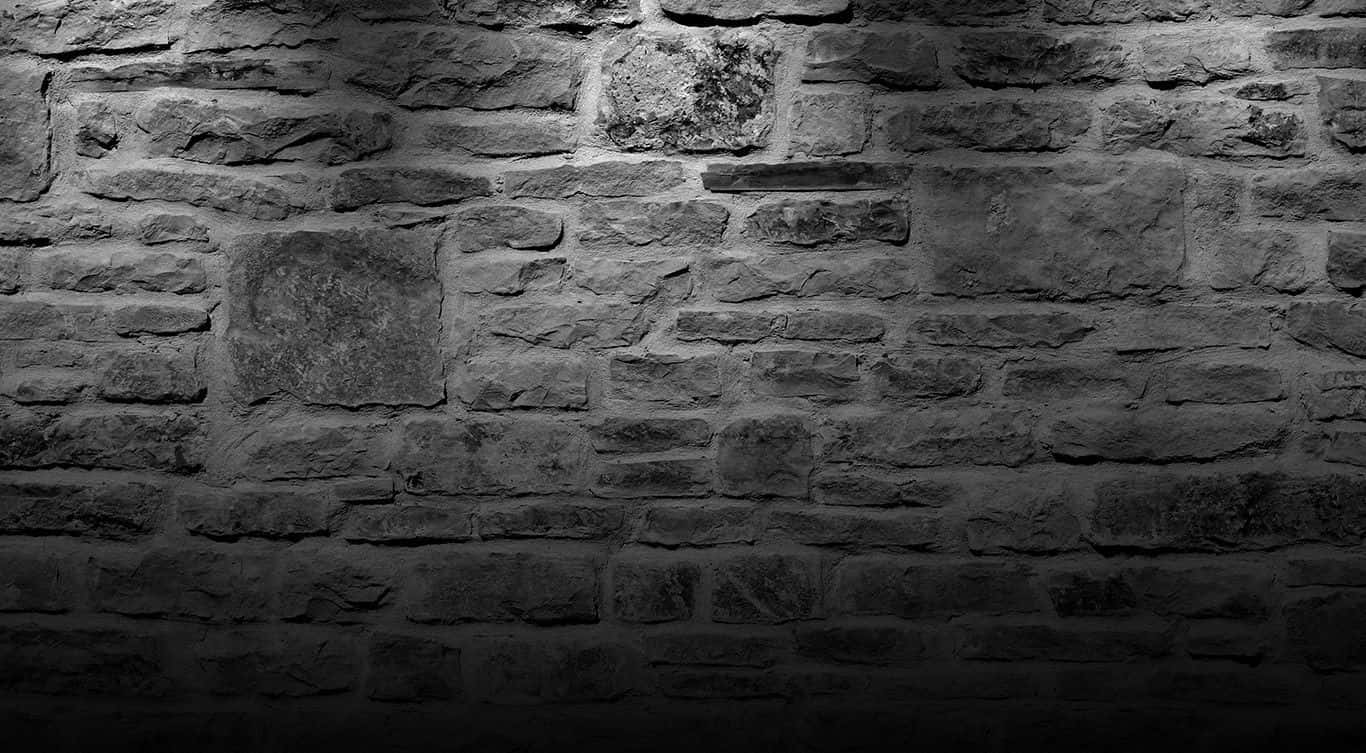 Dark Wall 桌布 壁紙 — 一面戲劇性的單色石牆，被聚光燈照亮，在其粗糙的紋理表面上投下深邃的陰影。