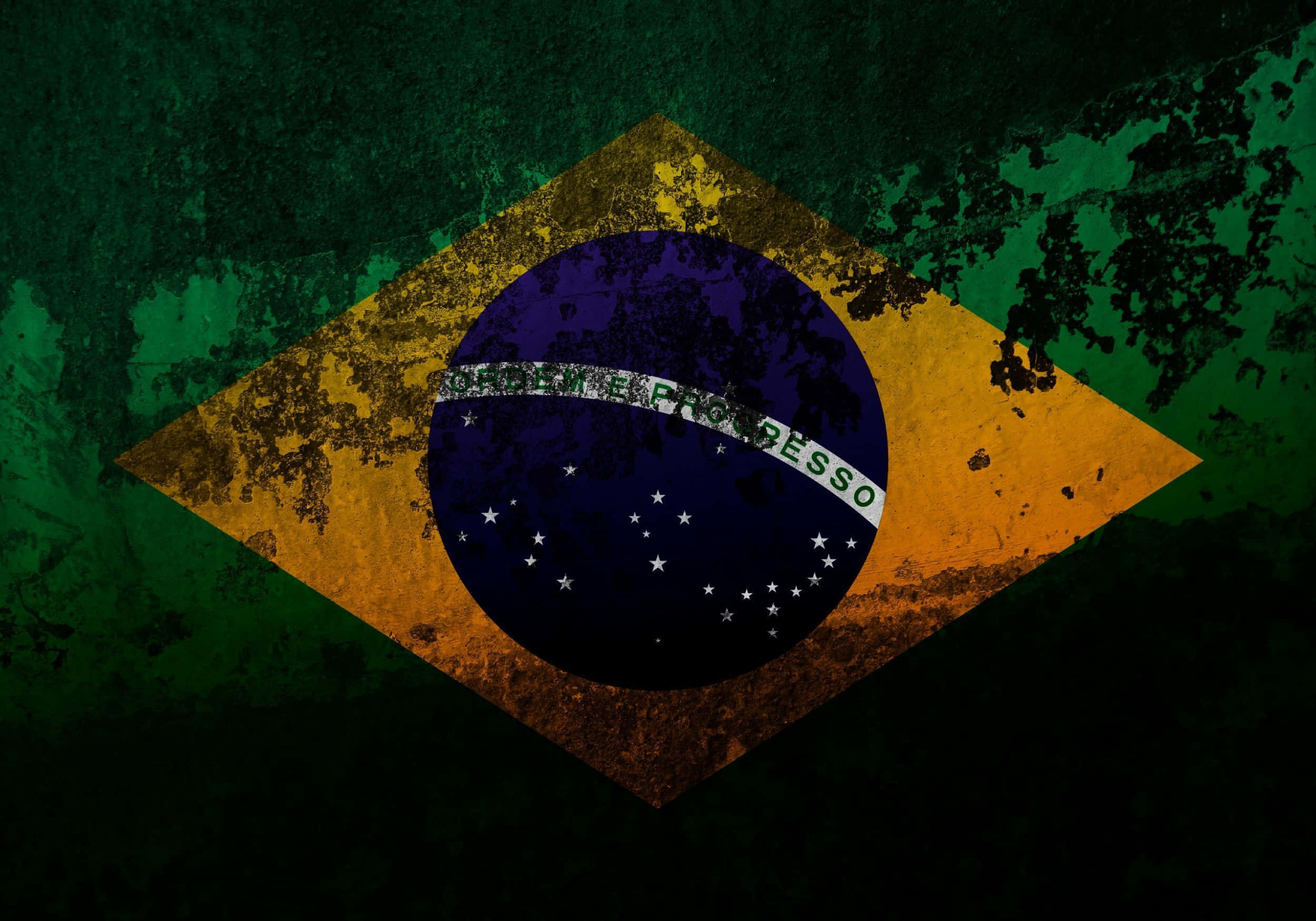 Brazil 桌布 壁紙 — 一面經風化的巴西國旗，帶有綠色、黃色、藍色和白色元素，置於深色紋理背景上。