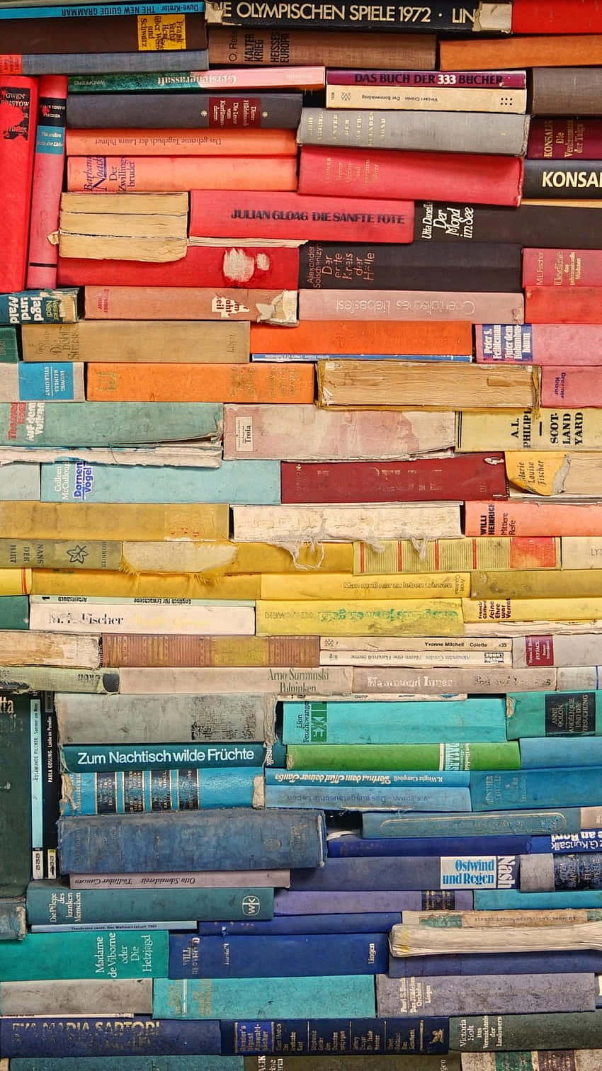 閱讀 桌布 壁紙 — 一面色彩繽紛、堆疊著各種顏色和磨損書脊的復古書籍牆，創造出有質感的文學拼貼畫。