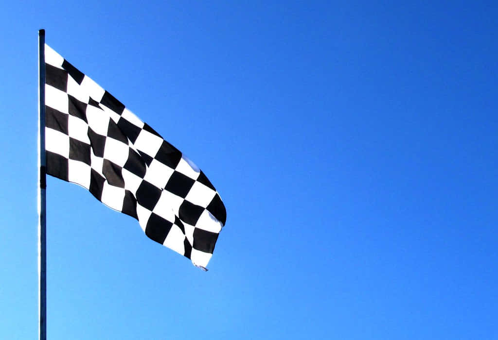 Chequered Flag 桌布 壁紙 — 一面黑白格仔賽車旗在晴朗的藍天下動態飄揚。