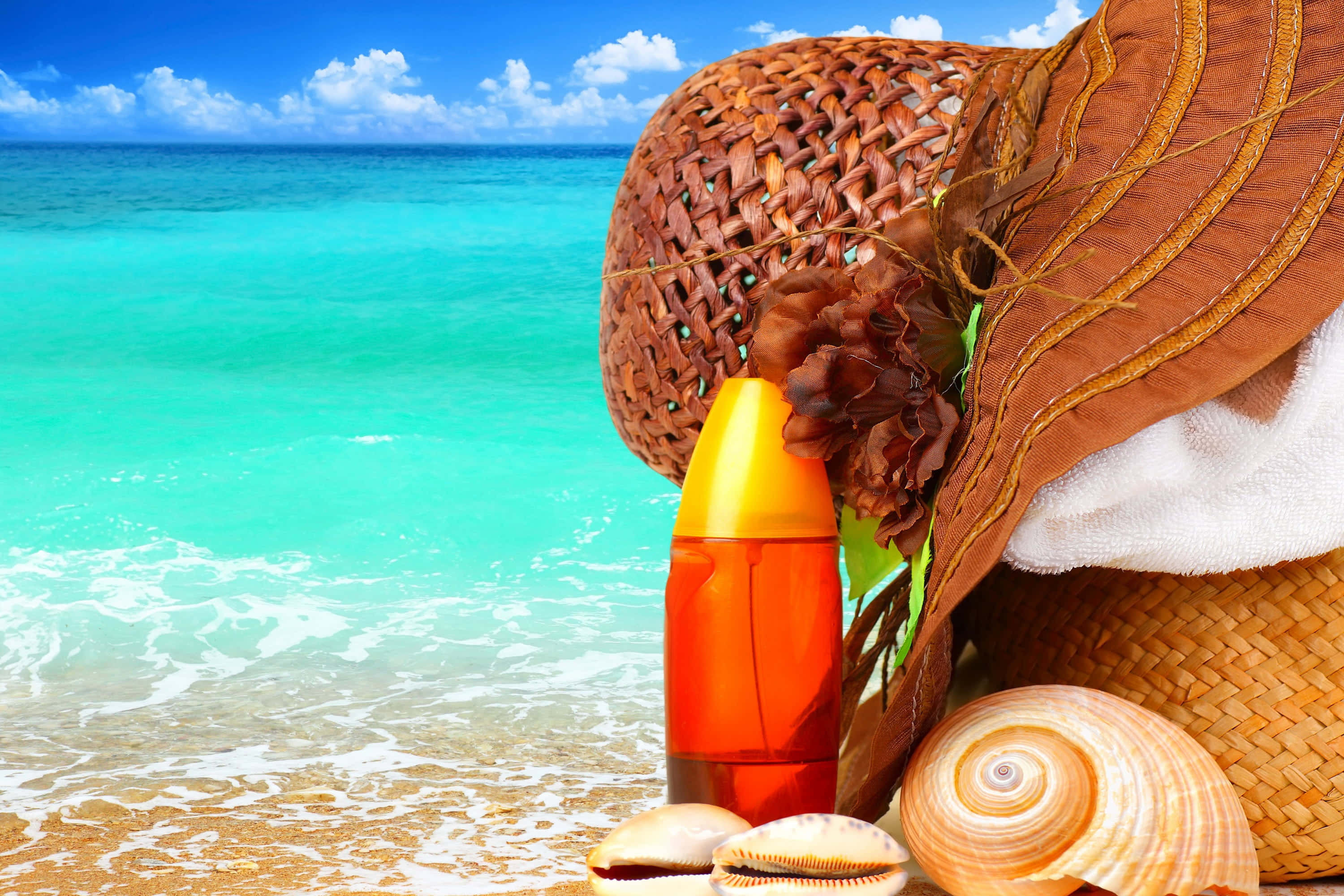 Beach Bag 桌布 壁紙 — 一頂太陽帽、防曬霜瓶和貝殼放在金色沙灘上，旁邊是碧綠的海浪，上方是明亮的藍天。