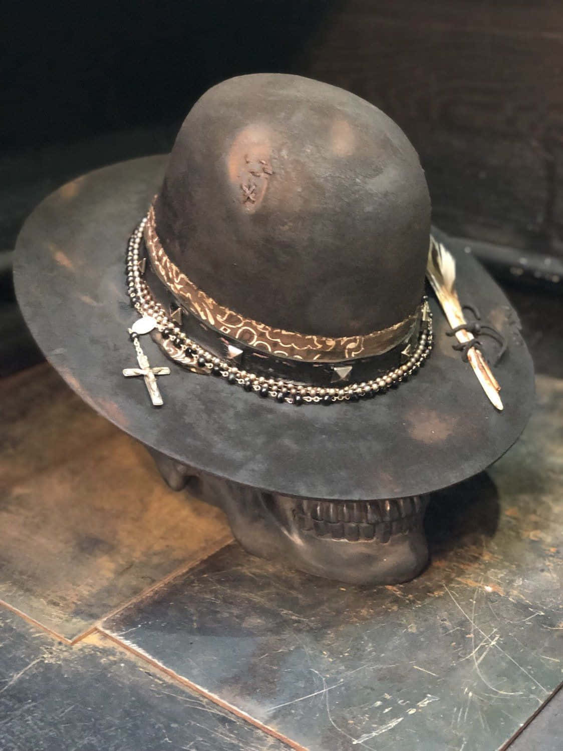 Hat 桌布 壁紙 — 一頂深色圓頂禮帽飾有鏈條、十字架和羽毛，擱在瓷磚表面上的頭骨上。