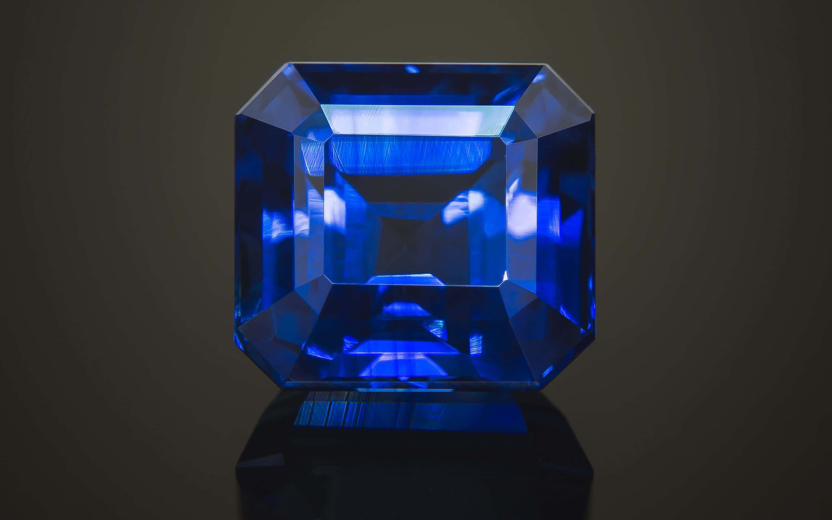 Sapphire Blue 桌布 壁紙 — 一顆令人驚嘆的深藍色祖母綠切割寶石在黑暗背景下閃耀著內部反射。