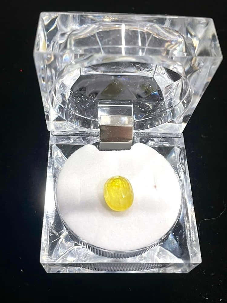 Yellow Sapphire 桌布 壁紙 — 一顆充滿活力的黃色寶石放在黑色背景前一個打開的水晶珠寶盒內的白色天鵝絨上。