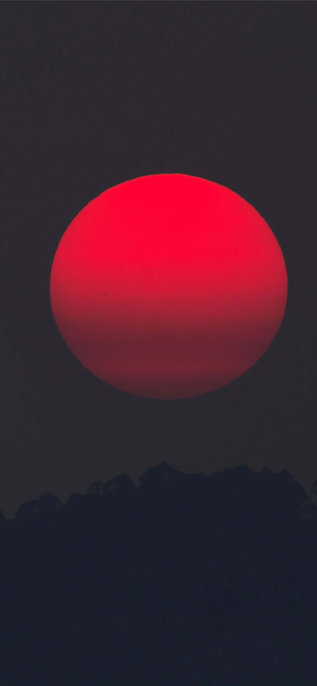 紅色 iPhone 壁紙 桌布 壁紙 — 一顆巨大的熾熱紅太陽主宰著黃昏時分黑暗天空中輪廓分明的山峰。
