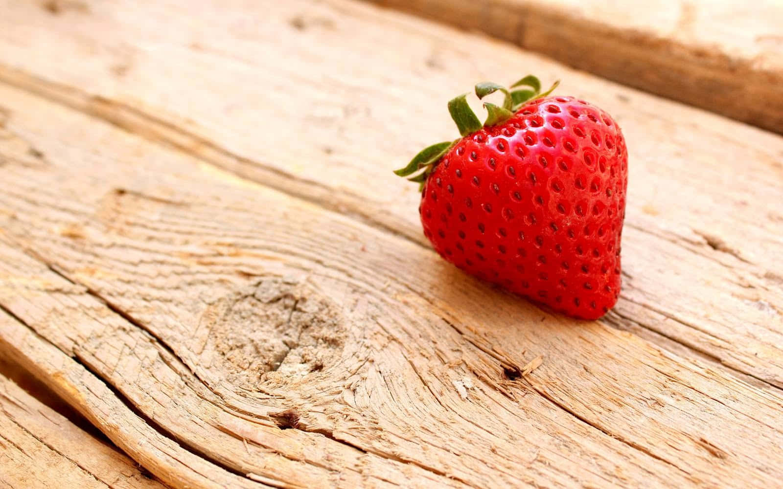 Cute Strawberry 桌布 壁紙 — 一顆成熟的紅色草莓，帶有綠葉，放在風化的木板上。