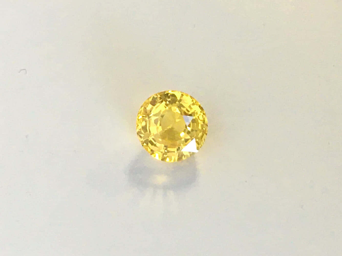 Yellow Sapphire 桌布 壁紙 — 一顆明亮的黃色圓形切割寶石在純白背景上閃爍著刻面。