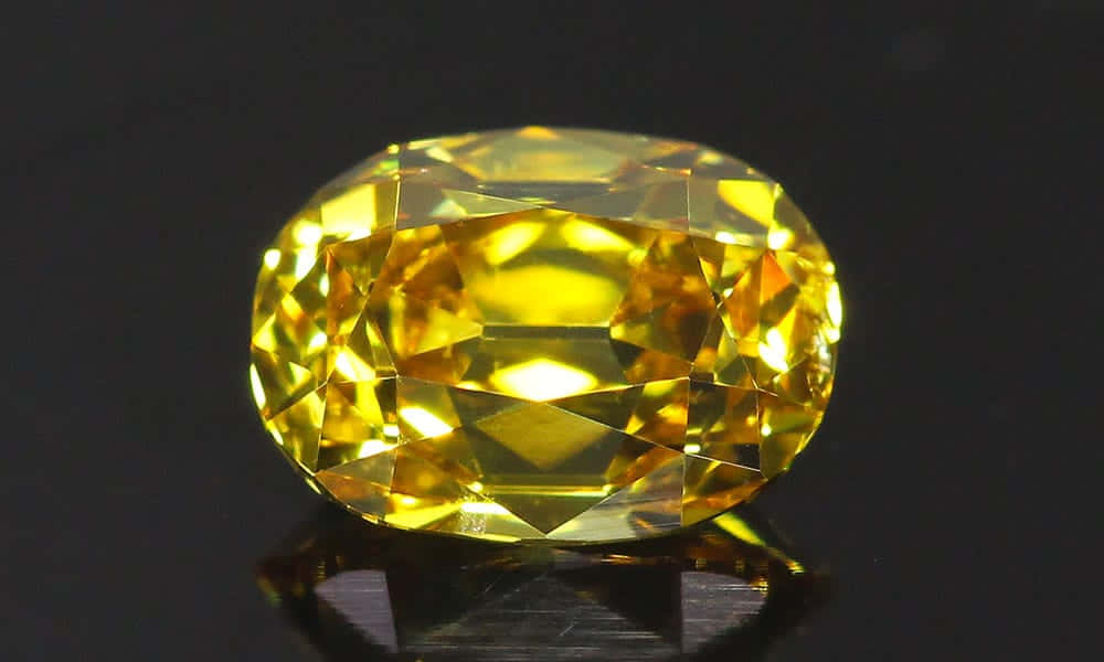 Yellow Diamond 桌布 壁紙 — 一顆明亮的黃色橢圓形切割寶石，在漆黑的反射表面上閃耀著火彩般的刻面。