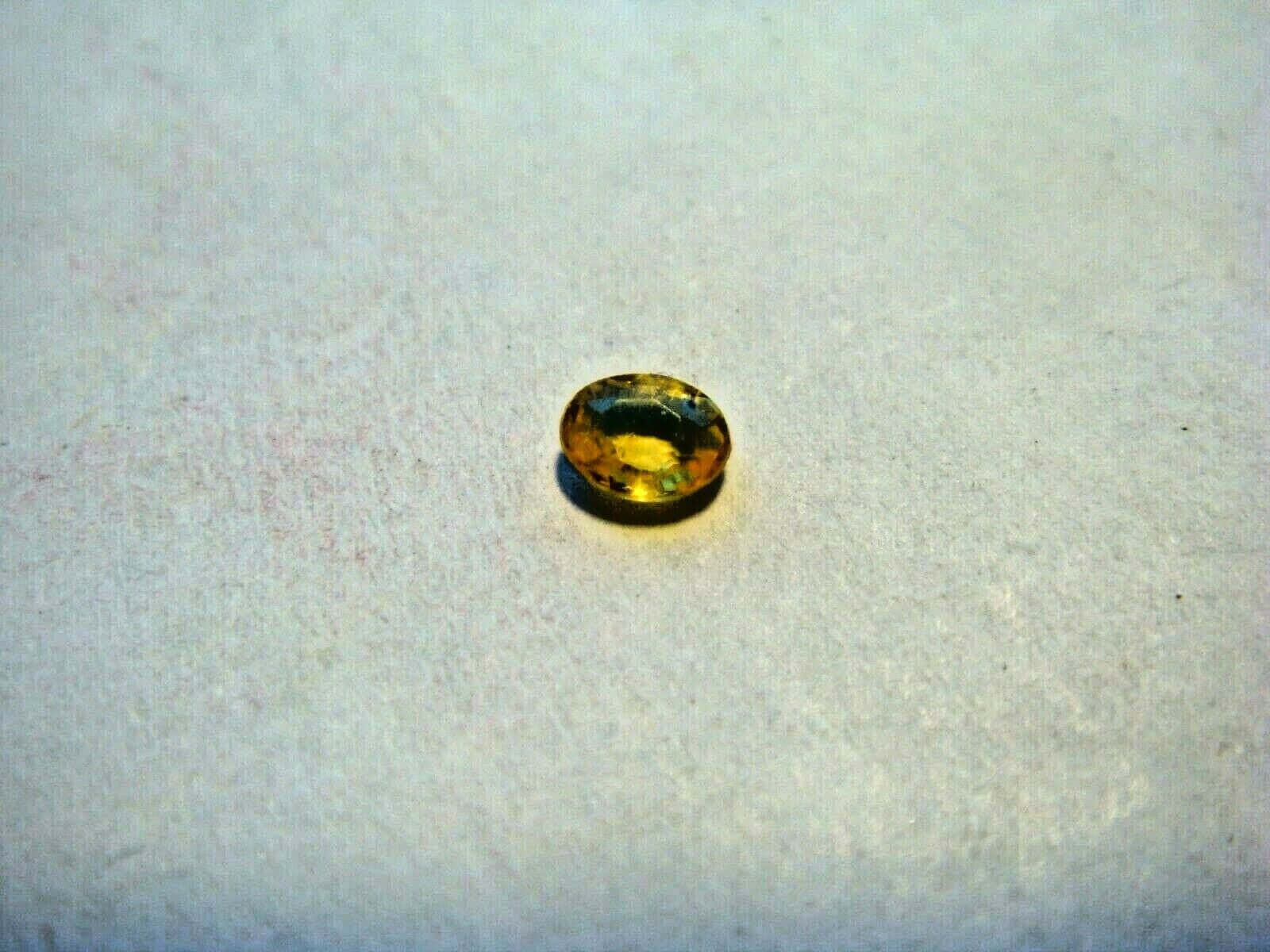 Yellow Sapphire 桌布 壁紙 — 一顆橢圓形切割的黃色寶石放置在帶有紋理的米白色表面上，捕捉光線並產生溫暖的內部反射。