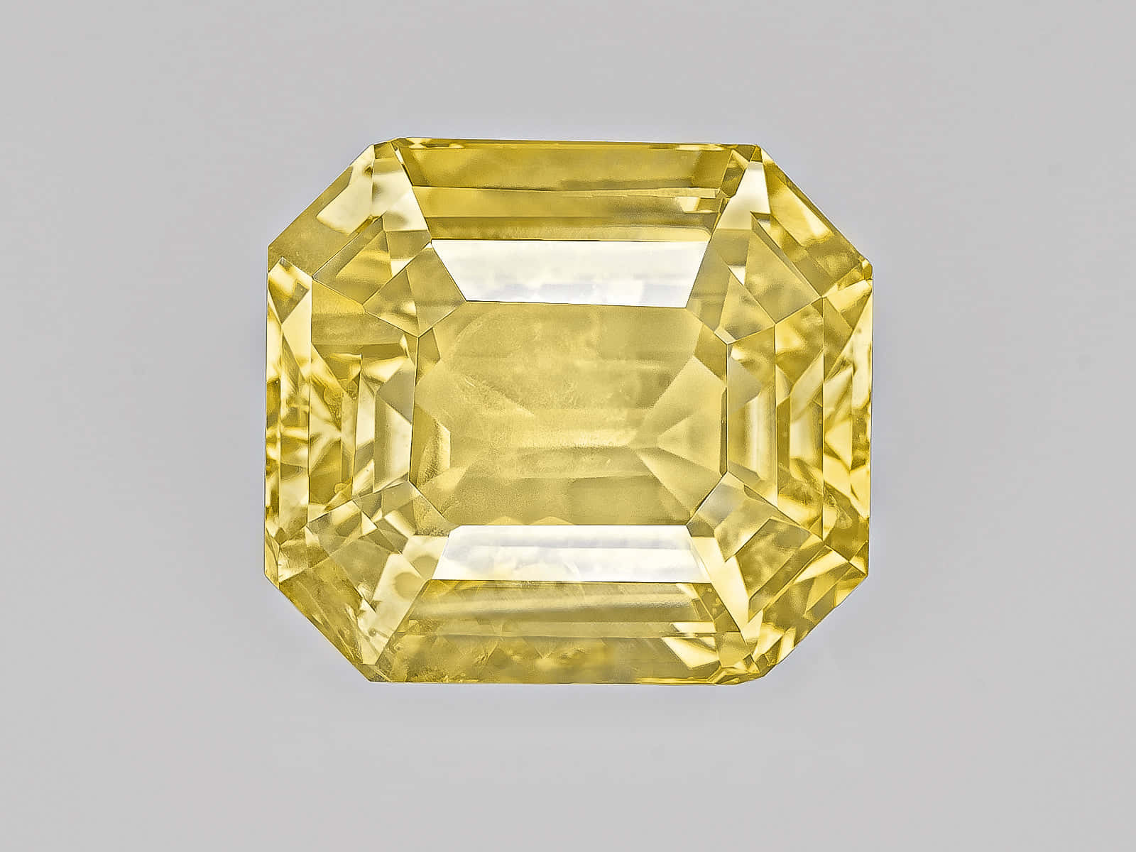 Yellow Sapphire 桌布 壁紙 — 一顆璀璨的黃色祖母綠切割鑽石，在灰色背景上閃耀著精確的刻面。