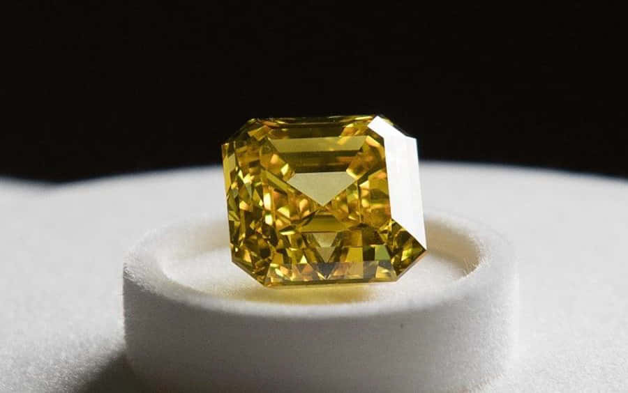 Yellow Diamond 桌布 壁紙 — 一顆璀璨的黃色祖母綠切割鑽石，在純黑背景上柔軟的白色墊子上閃耀著精準的刻面。
