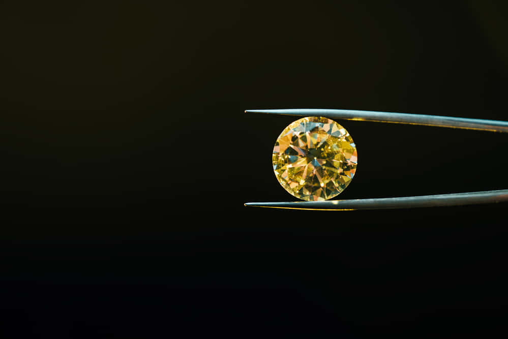 Yellow Diamond 桌布 壁紙 — 一顆璀璨的黃色鑽石被鑷子夾著，在純黑背景中閃耀。