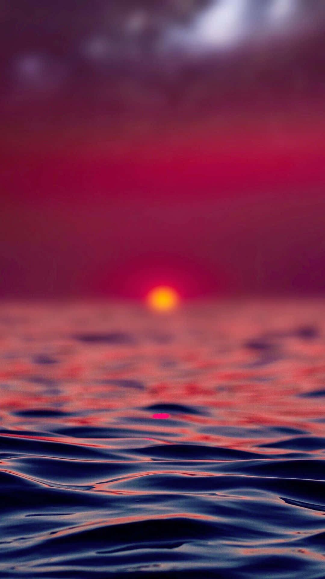 Portrait Mode 桌布 壁紙 — 一顆發光的橙色太陽在深紅色的天空下，沉入黑暗的海洋，柔和的漣漪反射著光線。