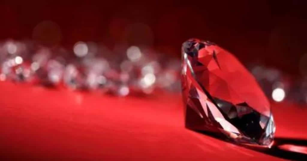 Red Diamond 桌布 壁紙 — 一顆紅色鑽石在深紅色背景上閃耀，背景遠處有模糊閃爍的寶石。
