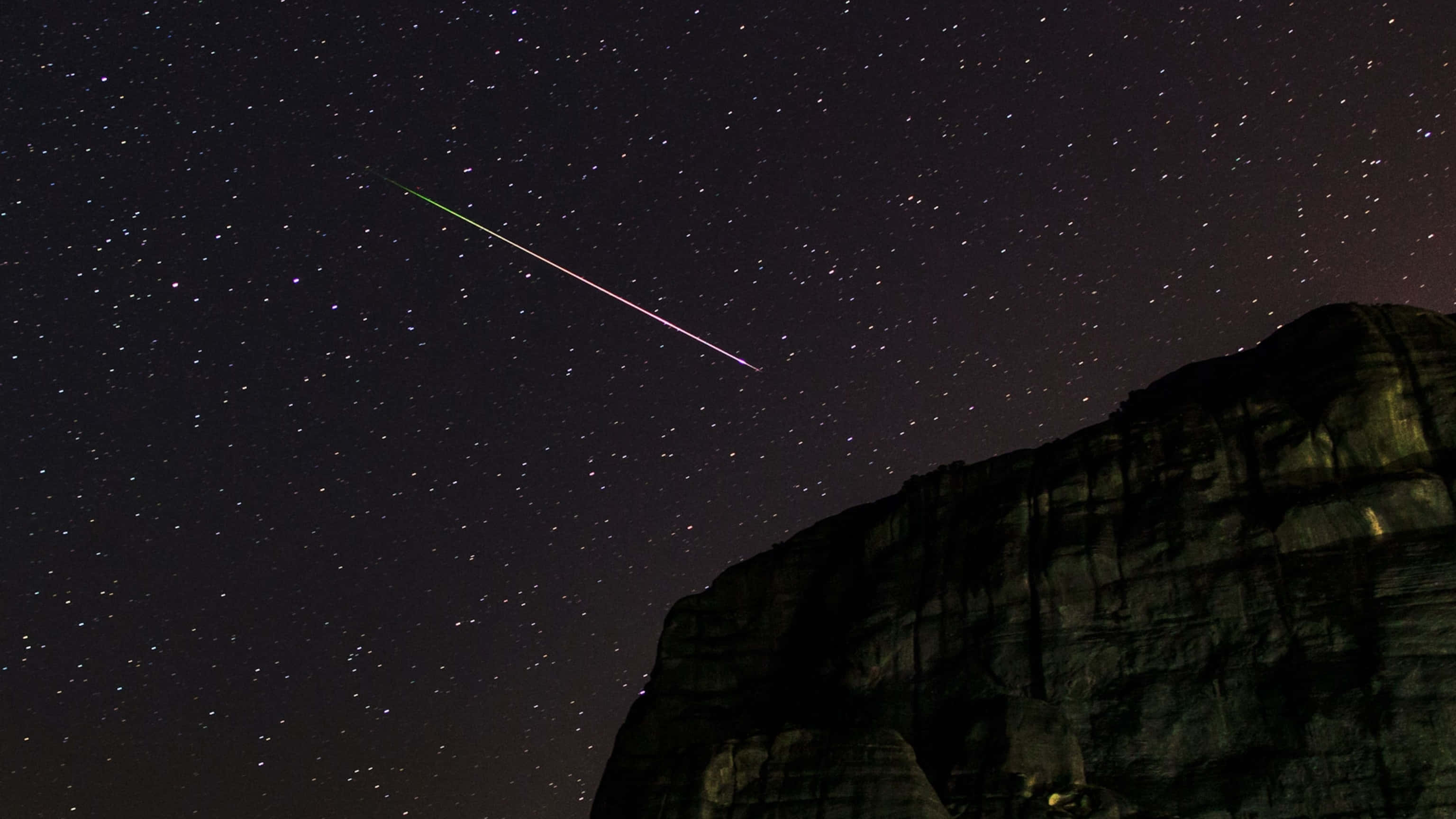 一顆絢爛流星劃過夜空 壁紙 — 一顆充滿活力的流星劃過崎嶇懸崖上方的星空夜空。