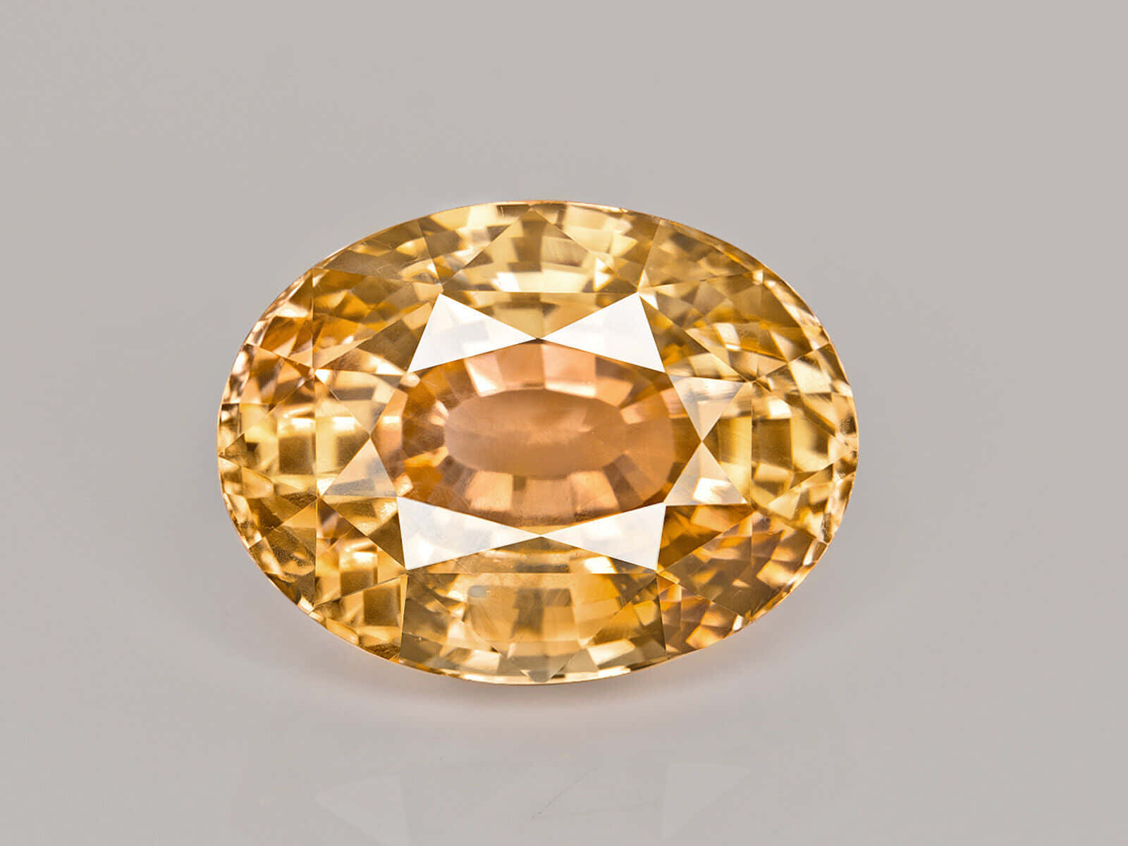 Yellow Sapphire 桌布 壁紙 — 一顆閃耀的橢圓形黃色寶石，帶有精細切割面，在灰色中性背景上閃爍光芒。