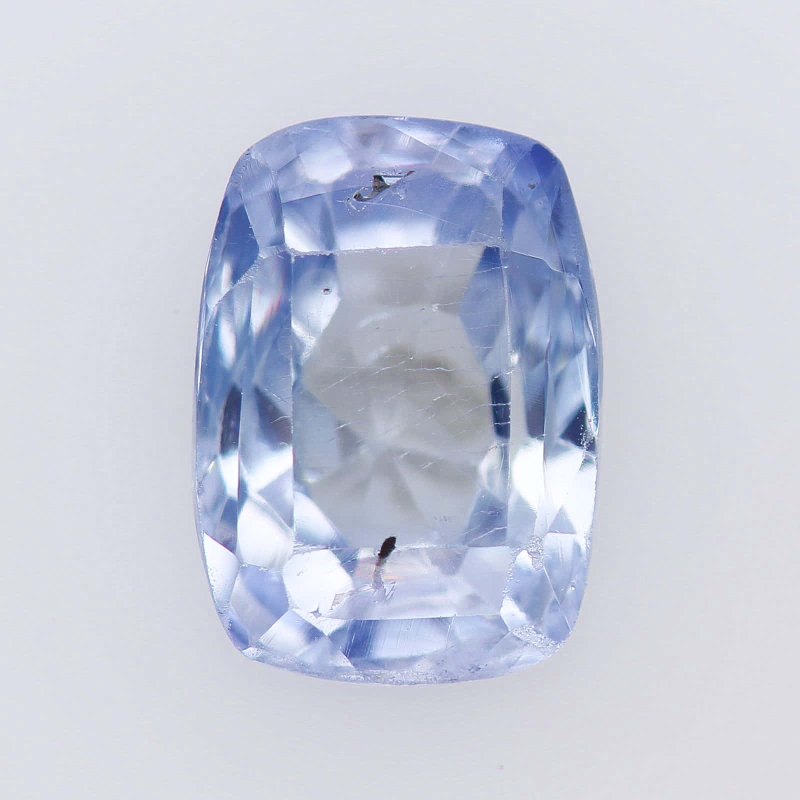 Periwinkle Blue 桌布 壁紙 — 一顆閃耀的淺藍色枕形切割藍寶石，帶有可見的內含物，置於純白色背景上。