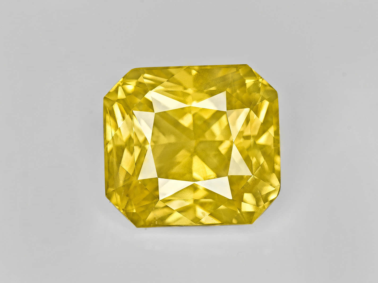 Yellow Sapphire 桌布 壁紙 — 一顆閃耀的黃色枕形切割鑽石，在灰色中性背景上展現精確的切面光芒。