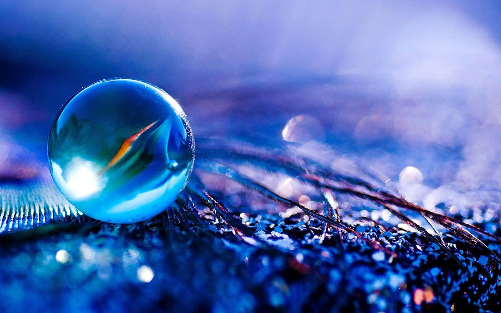3d Water 桌布 壁紙 — 一顆閃閃發光的藍色玻璃球體放置在紋理表面上，反射出鮮豔的光線和抽象的周圍環境。