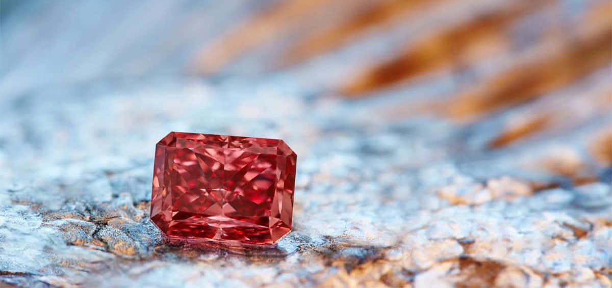 Red Diamond 桌布 壁紙 — 一顆鮮紅色長方形切割鑽石在帶紋理的藍色和橙色石頭表面上閃耀，景深較淺。