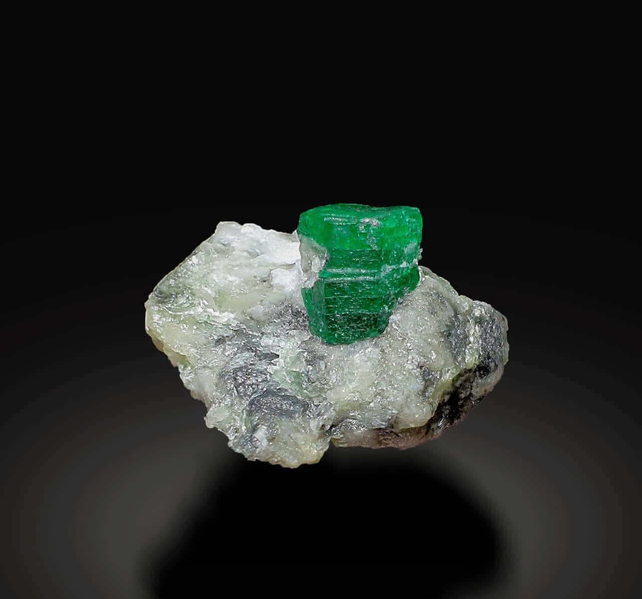 Emerald 桌布 壁紙 — 一顆鮮綠色嘅祖母綠晶體坐落喺粗糙嘅白色同灰色礦物基質上，背景係純黑色。