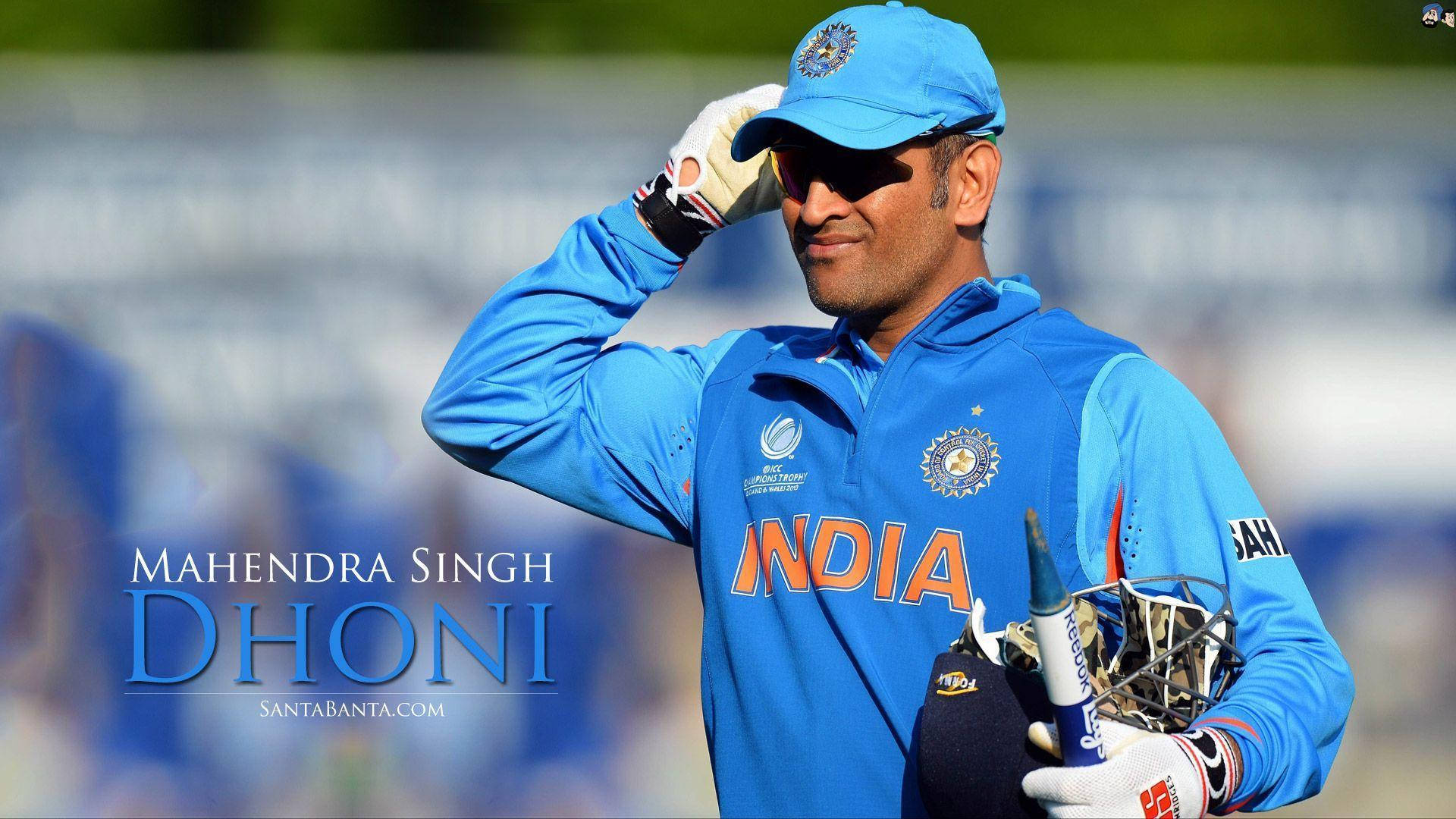 丁尼印度隊打擊手 壁紙 — Mahendra Singh Dhoni 穿著藍色印度板球裝備，在陽光明媚的場地上脫帽致意，手持球棒和頭盔。