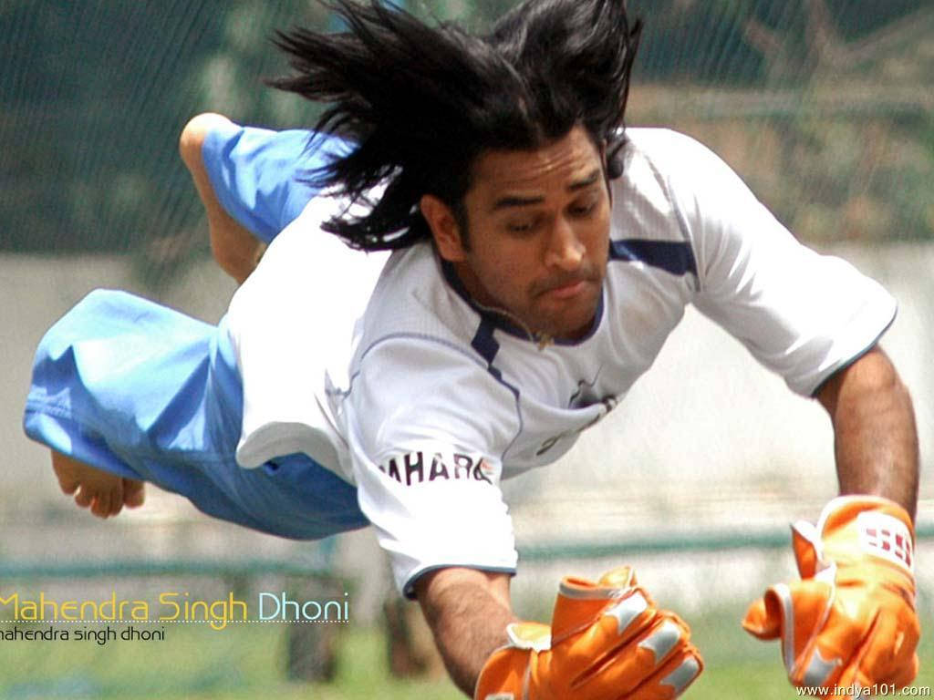 丁尼接球瞬間 壁紙 — 板球運動員 Mahendra Singh Dhoni 動態潛水，戴橙色手套和藍色短褲。