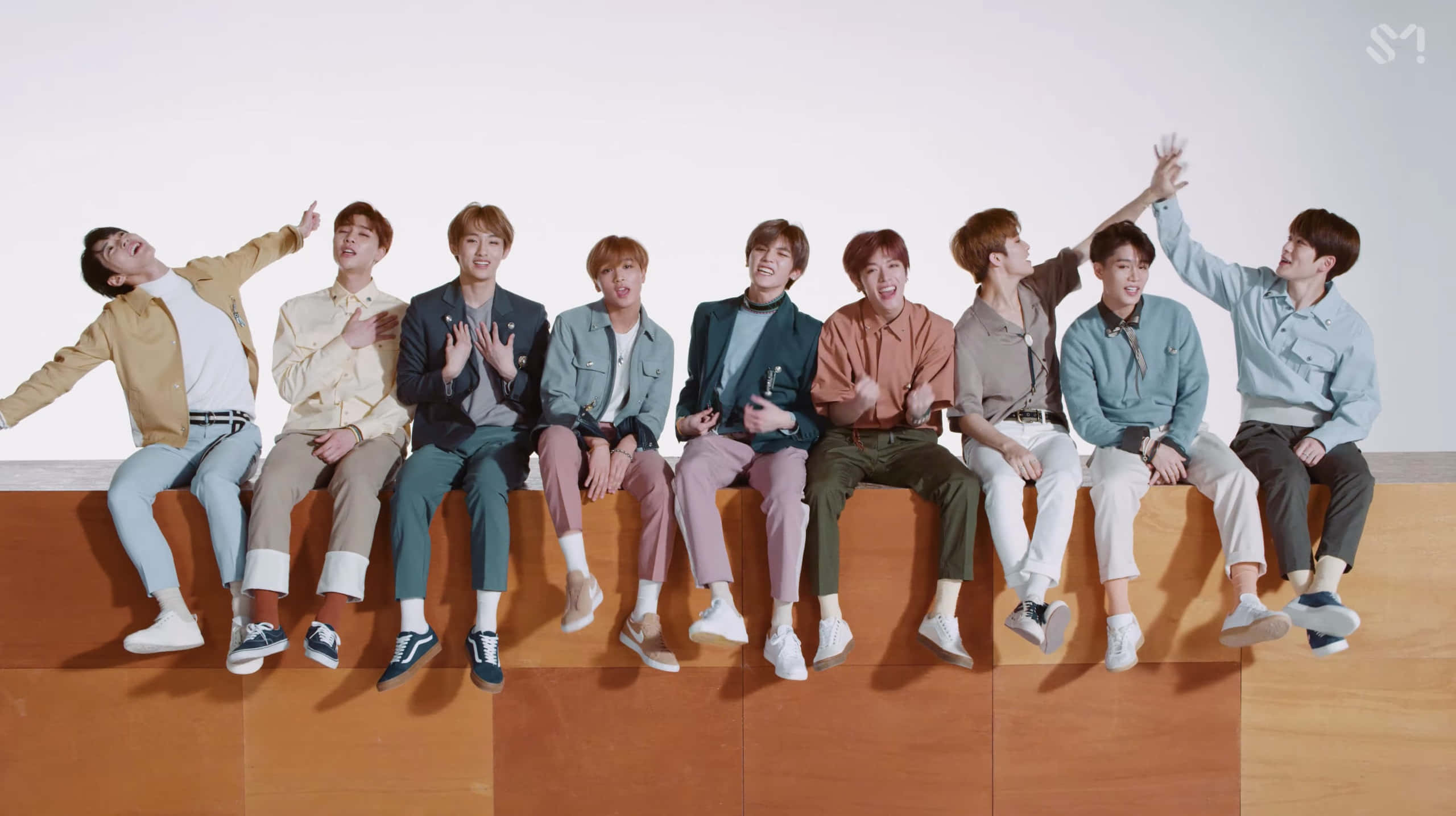 Nct 桌布 壁紙 — 七位年輕男士身穿時尚休閒服裝，坐在木質平台上，在純白背景前充滿活力地擺姿勢。