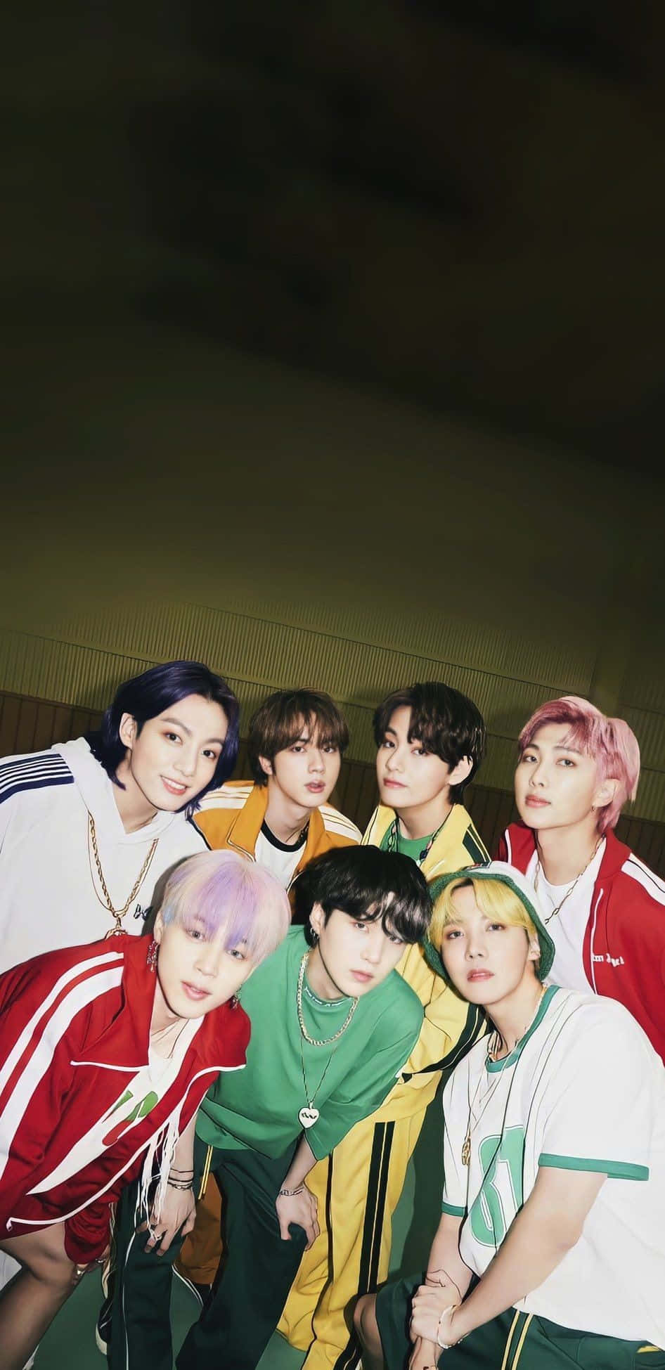 Bts Butter 桌布 壁紙 — 七位年輕男子，擁有色彩繽紛的頭髮和運動裝束，在昏暗的室內空間中緊密地擺姿勢。