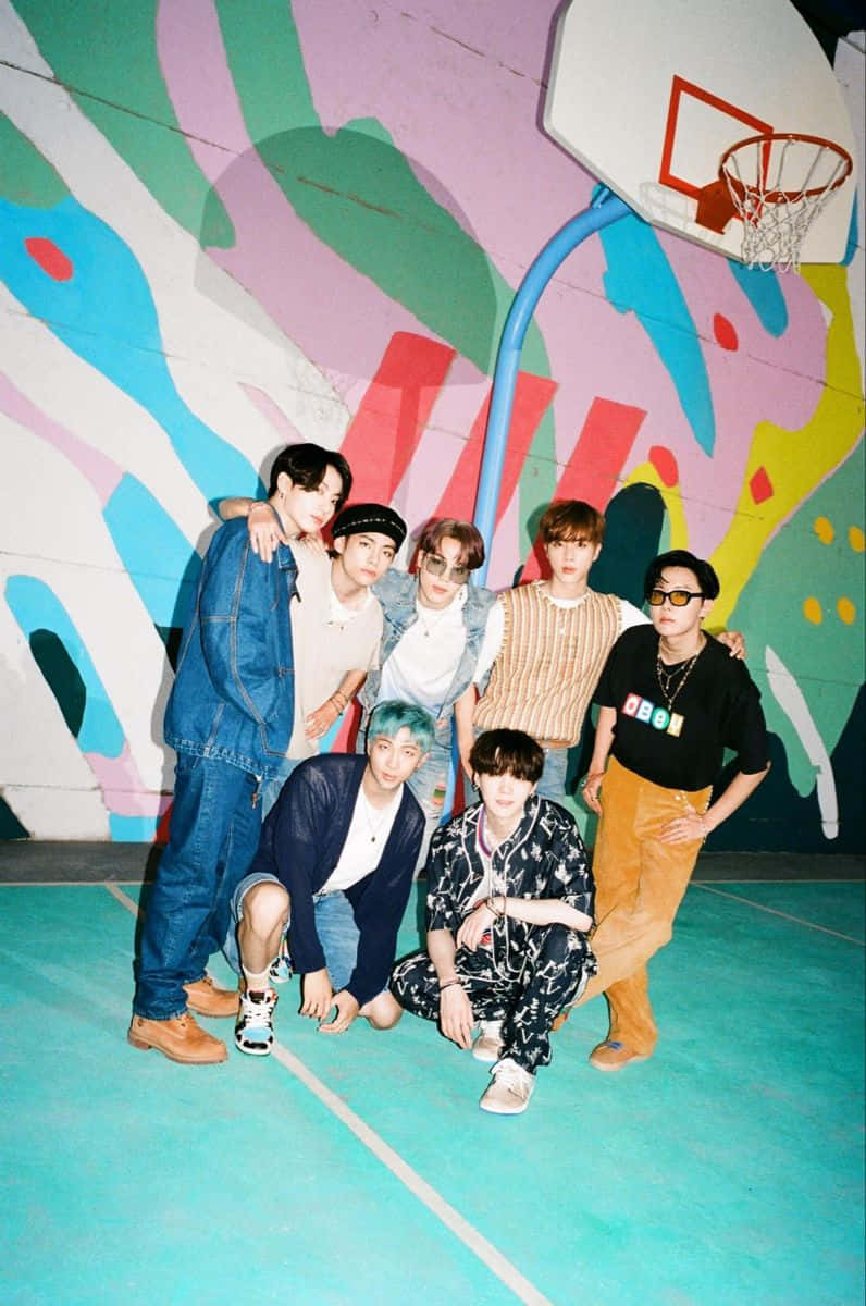 Big Hit Entertainment 桌布 壁紙 — 七位年輕男子在充滿活力的藍綠色籃球場上自信地擺姿勢，背景是色彩繽紛的抽象壁畫牆。