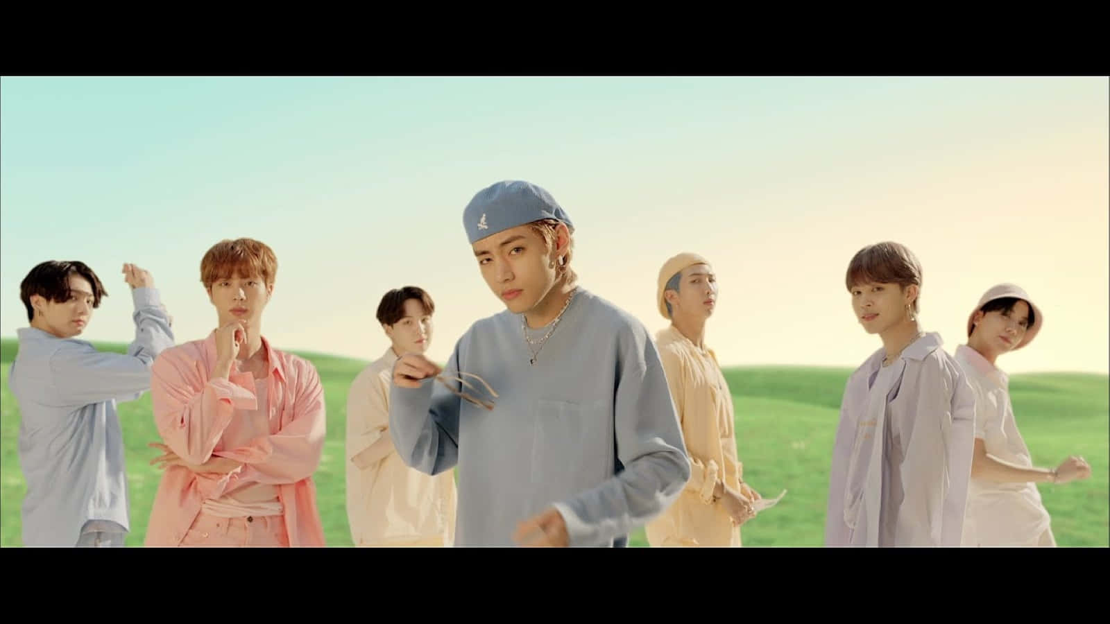 Bts Mv 桌布 壁紙 — 七位年輕男子身穿柔和色調服裝，在晴朗天空下的陽光綠地上自信擺姿勢。