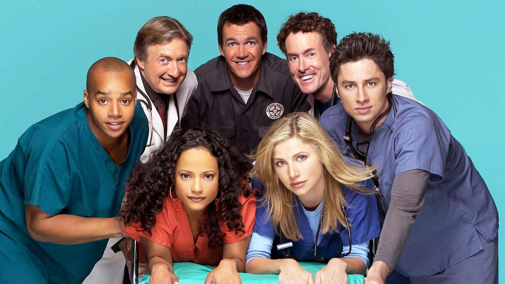 John C. Mcginley 桌布 壁紙 — 七位微笑的醫護人員穿著手術衣，在純青色背景前一起擺姿勢。