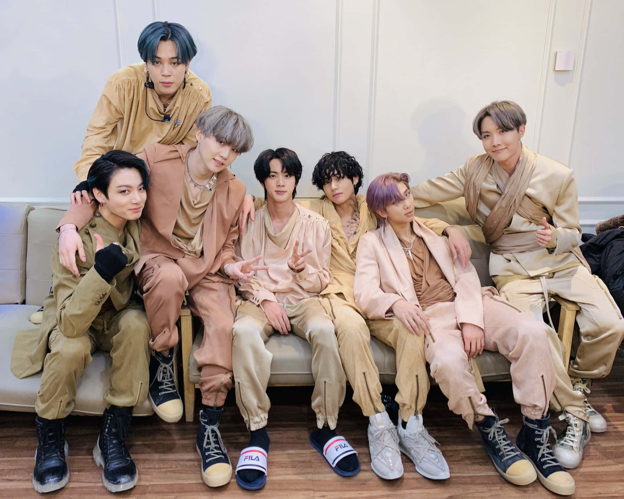 Big Hit Entertainment 桌布 壁紙 — 七位時尚年輕男士穿著協調的米色服裝，在沙發上以俏皮的姿態和自信的表情隨意擺姿勢。