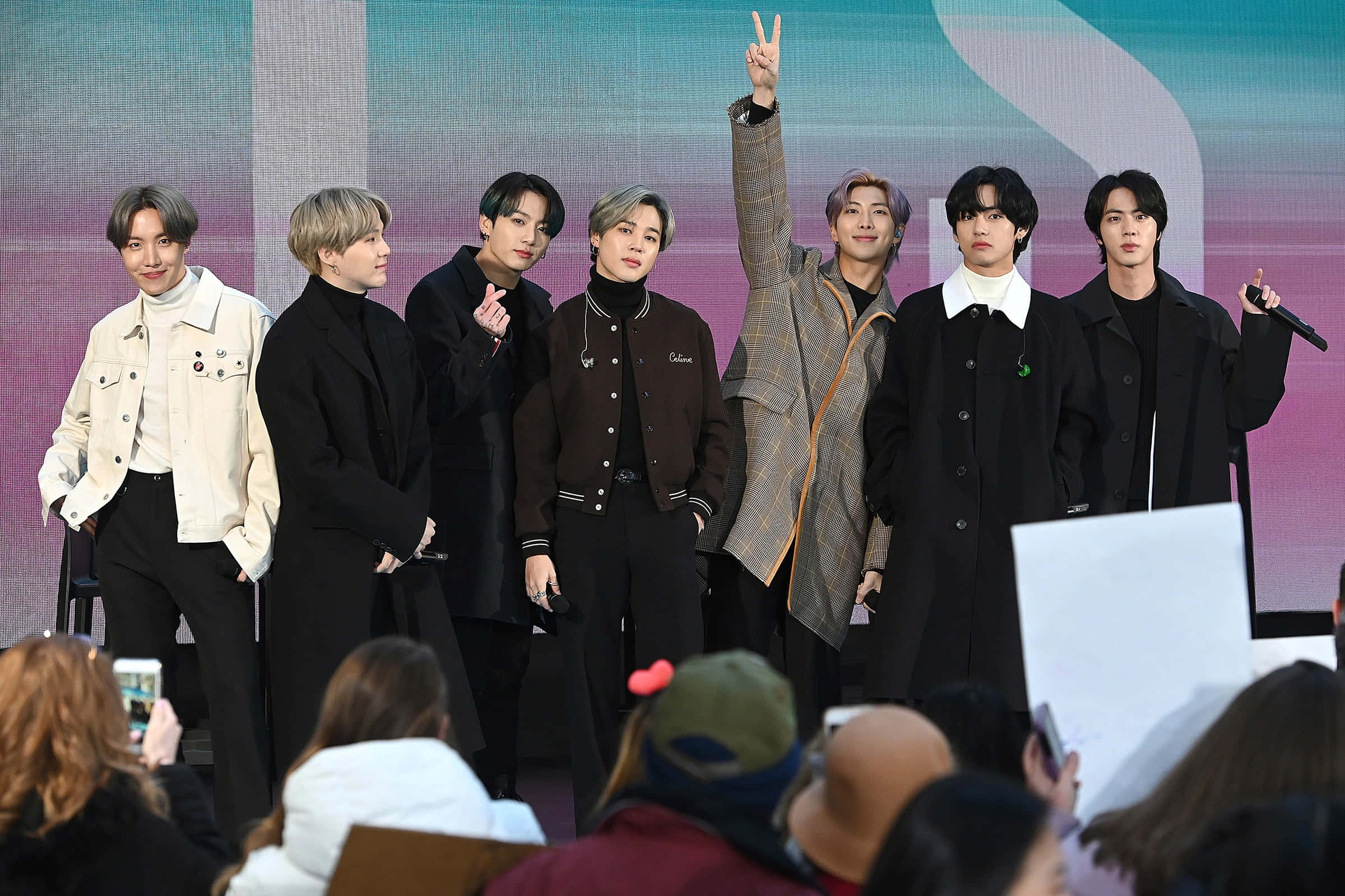 Bts Live 桌布 壁紙 — 七位時尚的男性偶像在舞台上自信地擺姿勢，前景的粉絲捕捉了這一刻。