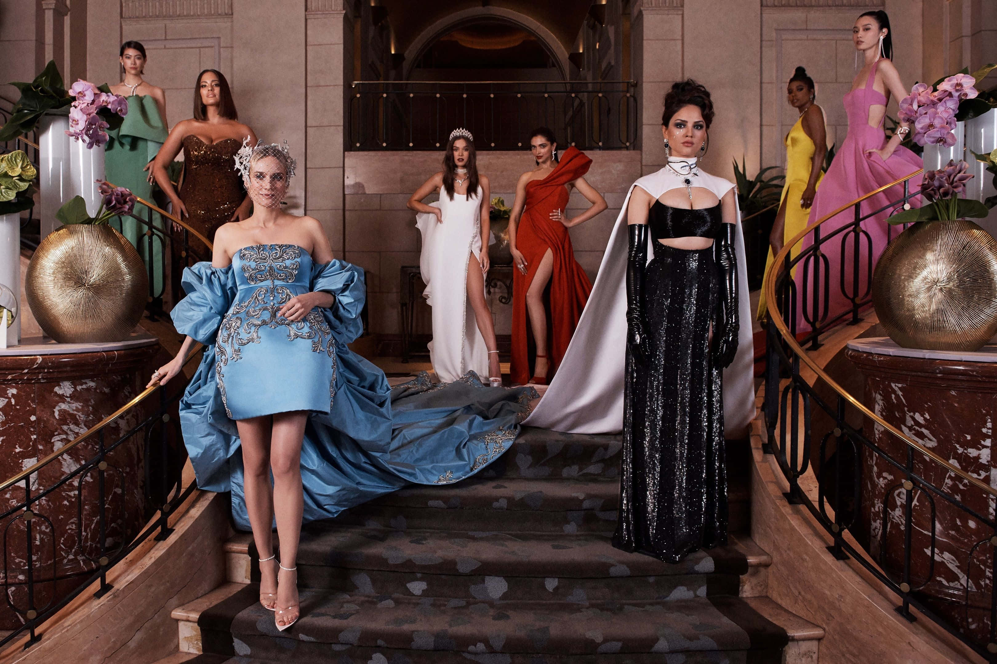 Met Gala 桌布 壁紙 — 七位模特兒身穿華麗禮服，在裝飾著超大型花卉佈置的宏偉大理石樓梯上優雅地擺姿勢。