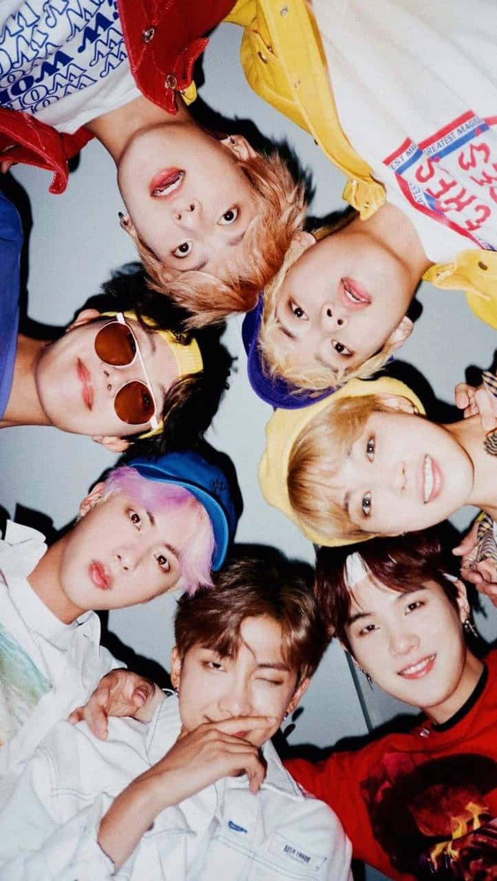 Bangtan Sonyeondan 桌布 壁紙 — 七位身穿色彩繽紛服裝的年輕男性在純色背景下緊密圍成一圈向上凝視。