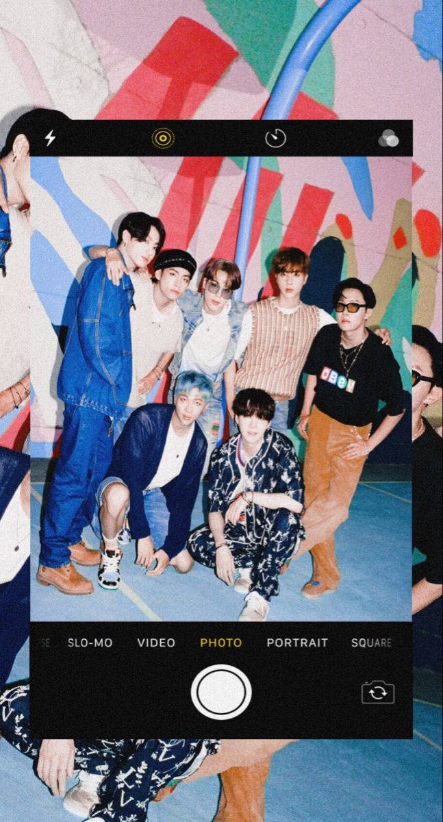 bts iPhone 桌布 壁紙 — 七個年輕男子在一個充滿活力的塗鴉房間裡隨意擺姿勢，由智能手機相機界面框住。