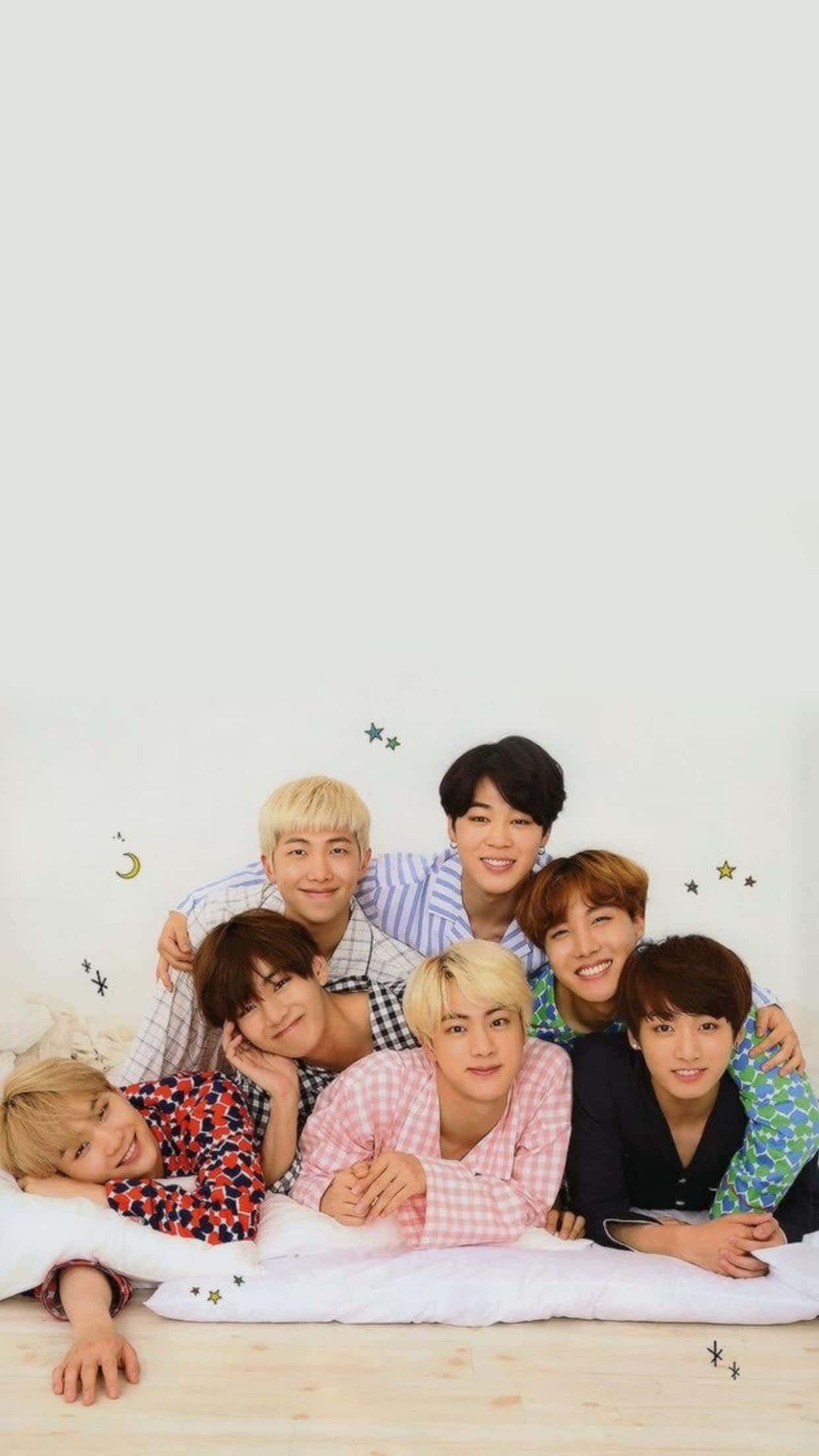 Bangtan Sonyeondan 桌布 壁紙 — 七個穿著睡衣的年輕男子在貼有星星和月亮貼紙的素牆前，在床上微笑並一起放鬆。