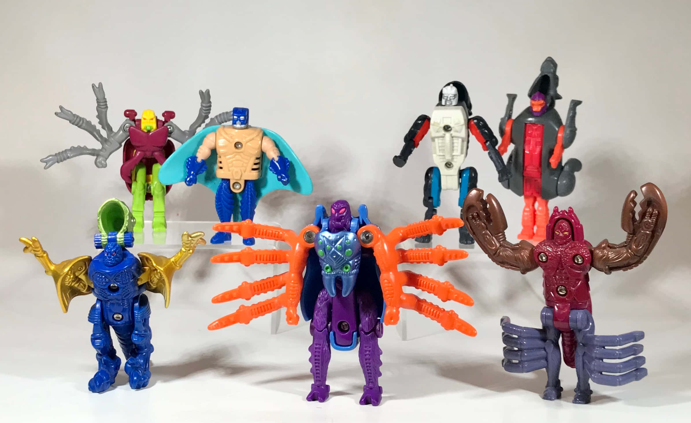 toys 桌布 壁紙 — 七個色彩繽紛的塑膠動作人偶，帶有昆蟲型和機械人設計，在純白色背景前擺出姿勢。