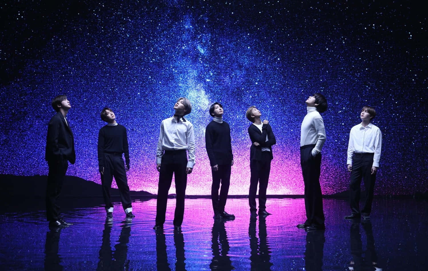 Bts Mv 桌布 壁紙 — 七名身穿正裝的男子站在反光表面上，仰望充滿紫色和藍色色調的 vibrant 宇宙星場。