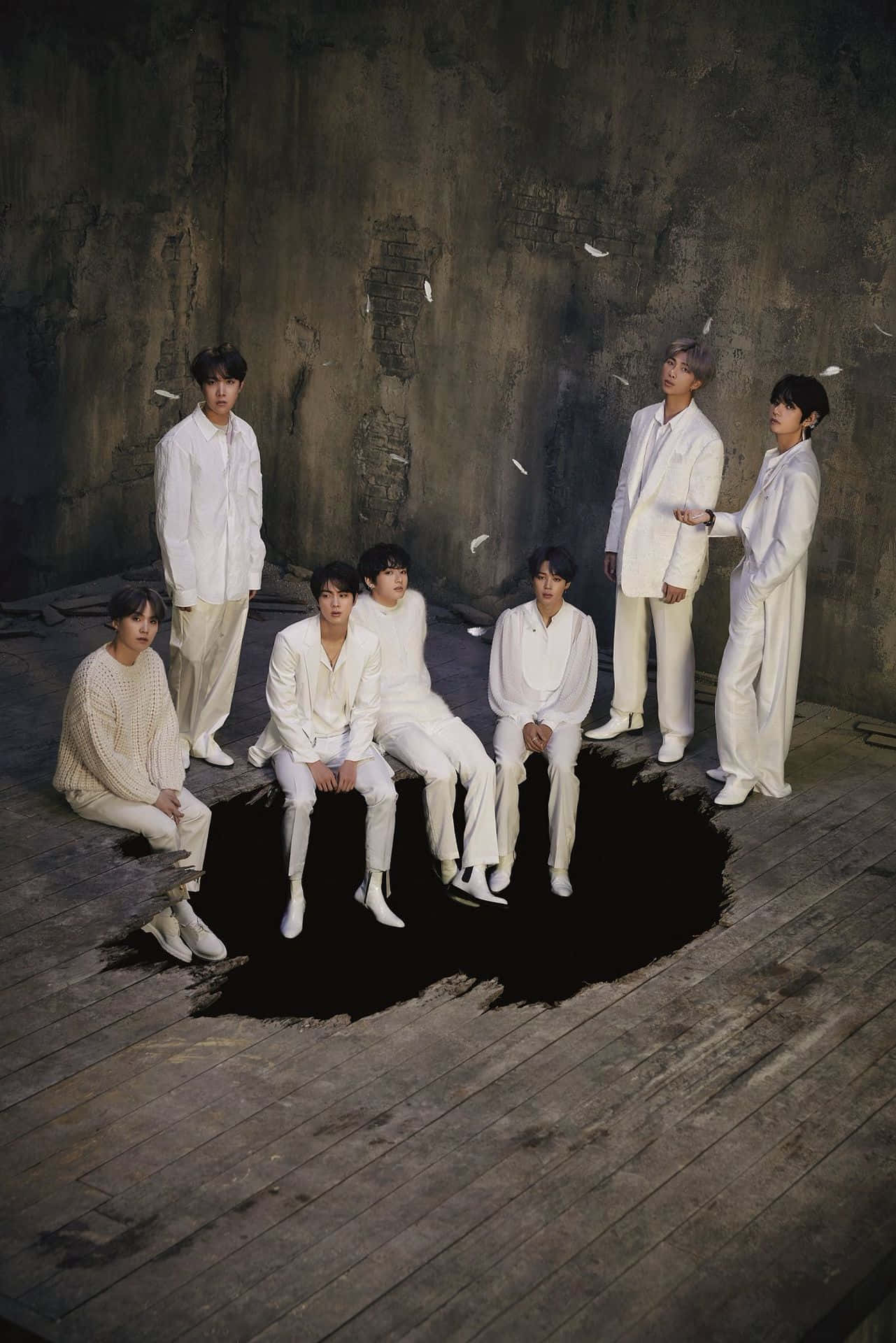 Big Hit Entertainment 桌布 壁紙 — 七名身穿白色服裝的男子，在一個風化木地板上的暗洞周圍擺姿勢，背景是帶紋理的灰色牆壁。