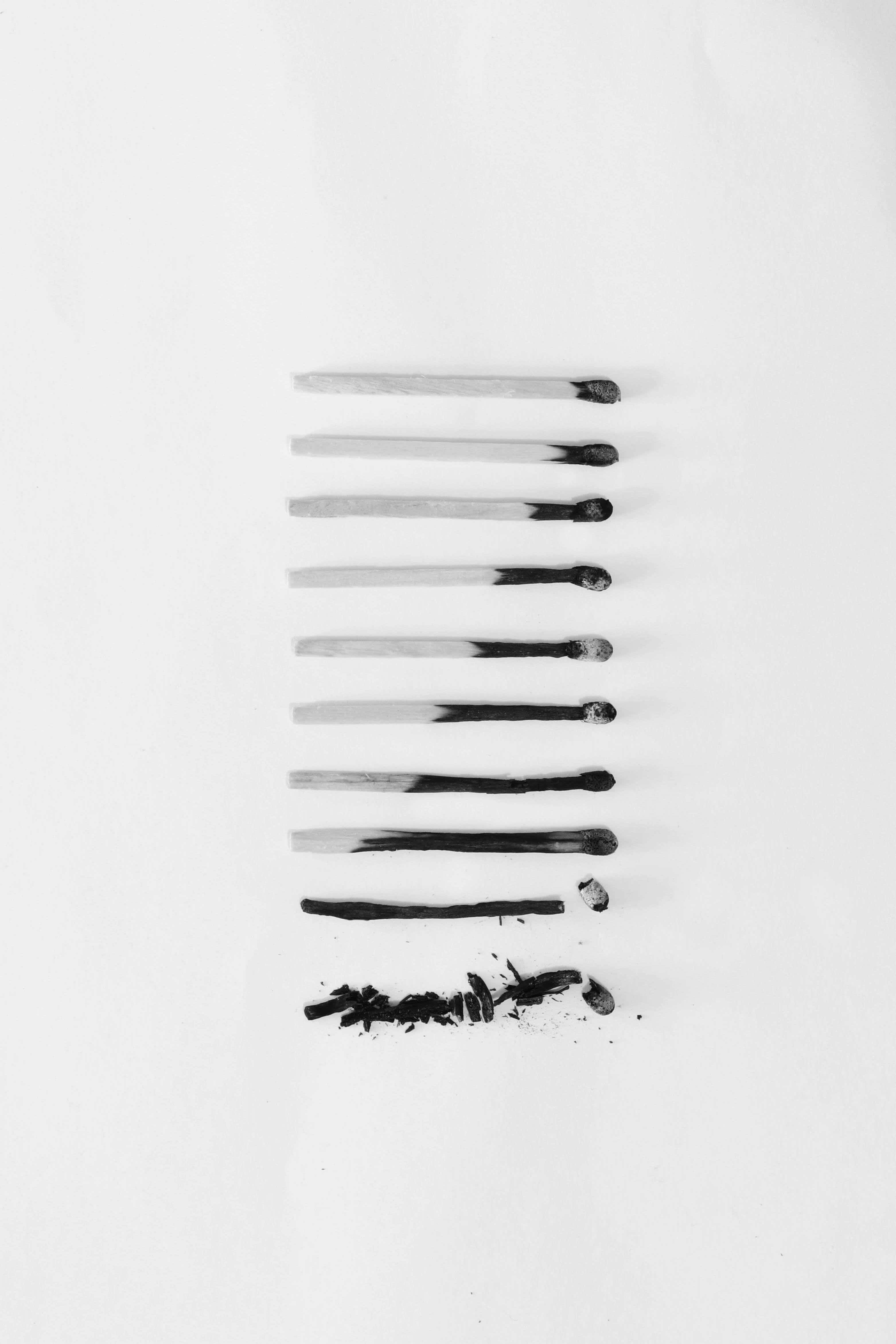 黑白美學 桌布 壁紙 — 七根燒過的火柴垂直排列在白色背景上，下方散落著灰燼。