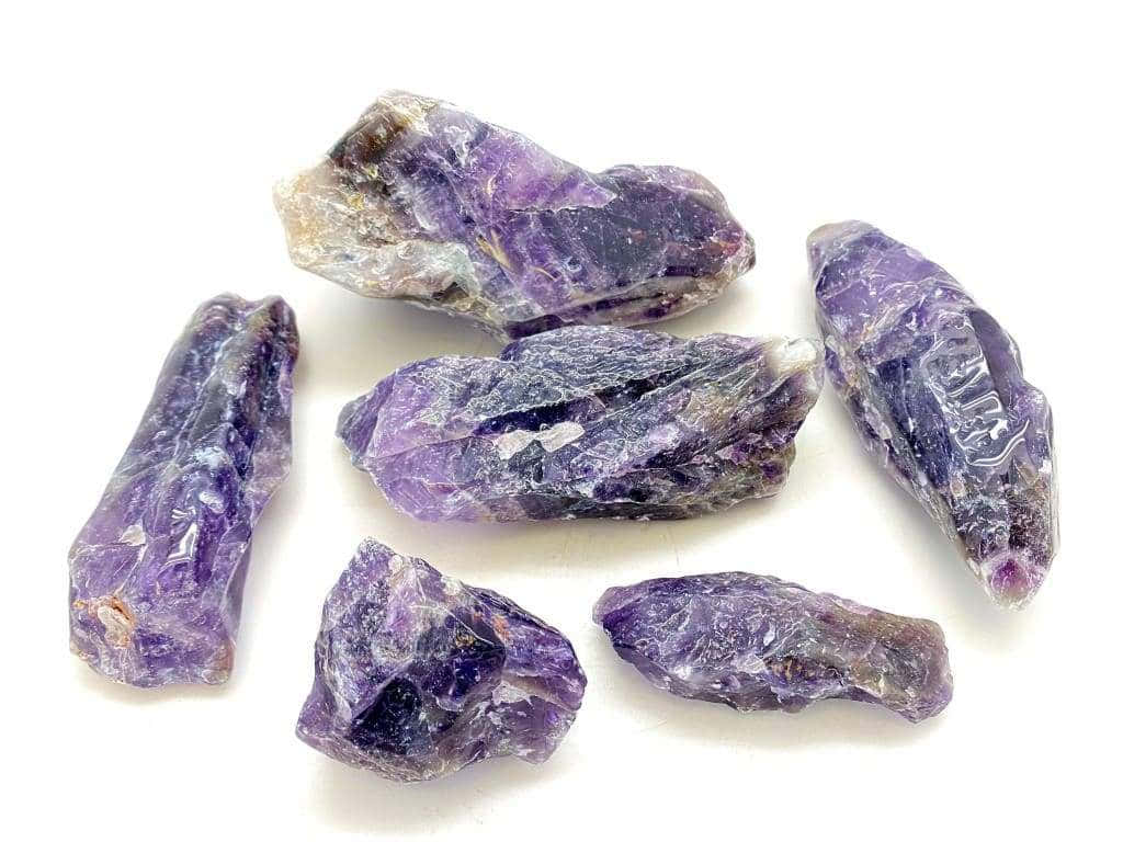 Amethyst 桌布 壁紙 — 七顆帶有深紫色和白色紋理的天然紫水晶原石，放置在明亮的白色表面上。
