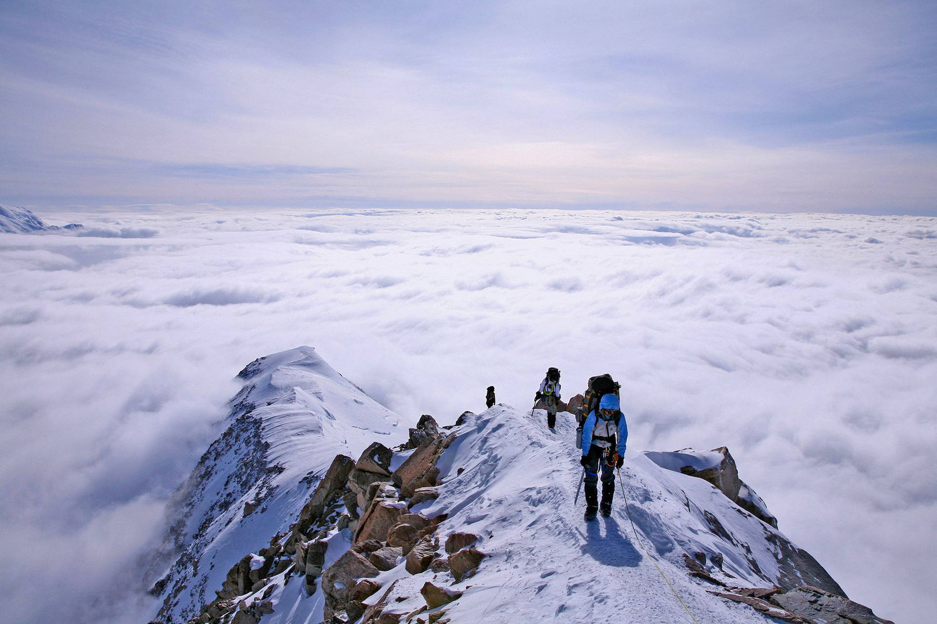 登山者在廣闊雲海之上的積雪山脊上徒步。