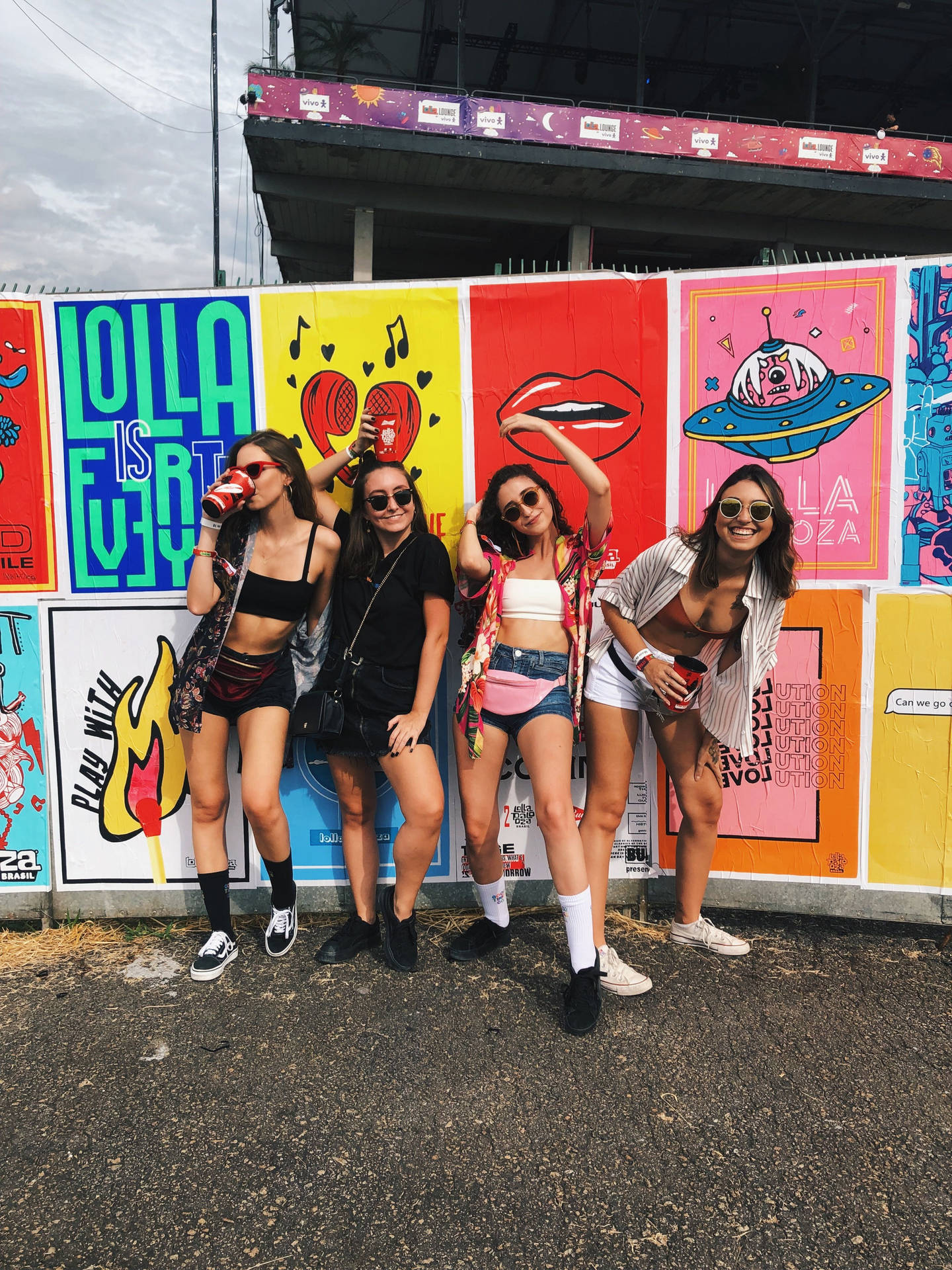 四位穿著節日服裝的年輕女性在色彩繽紛的音樂會海報前擺姿勢。