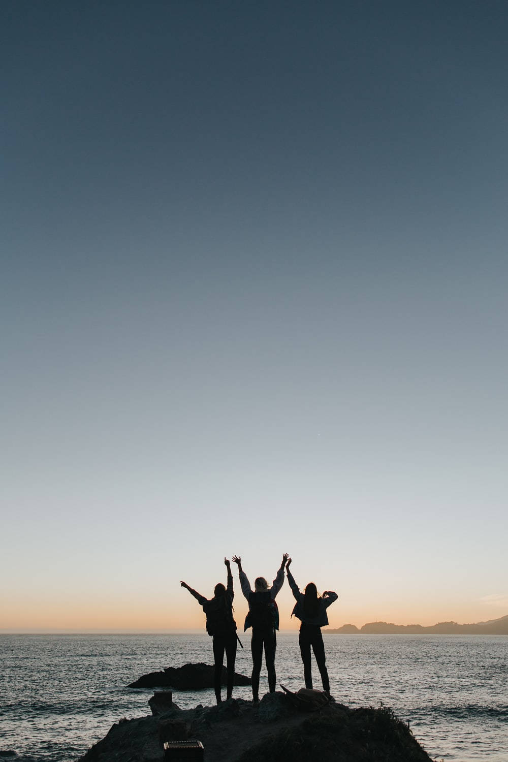 三人在日落時分在海邊懸崖邊緣慶祝。