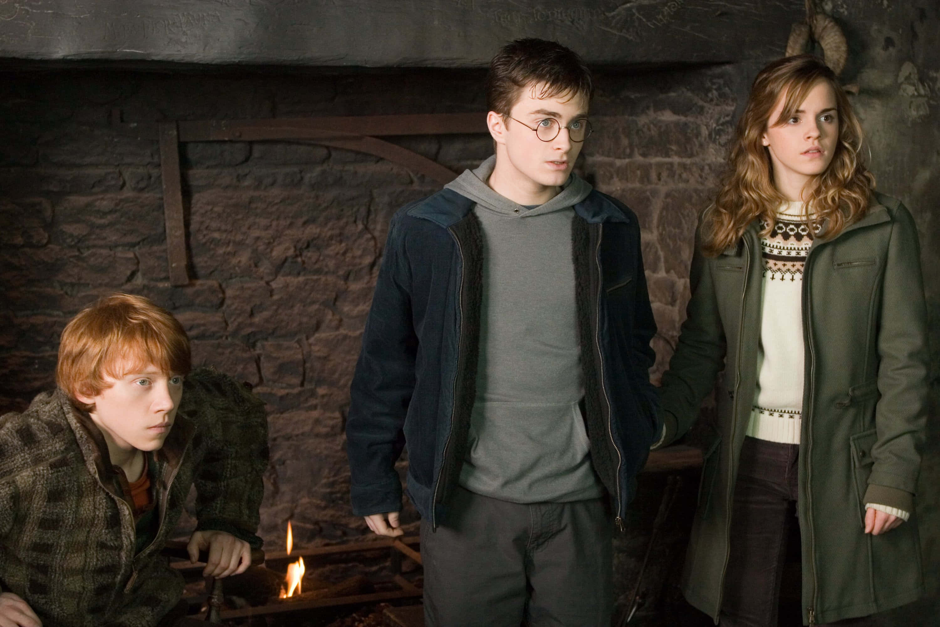 The Order Of Phoenix 桌布 壁紙 — 三位年輕巫師站在一個石牆房間裡，身後有噼啪作響的壁爐，他們看起來警覺而擔憂。