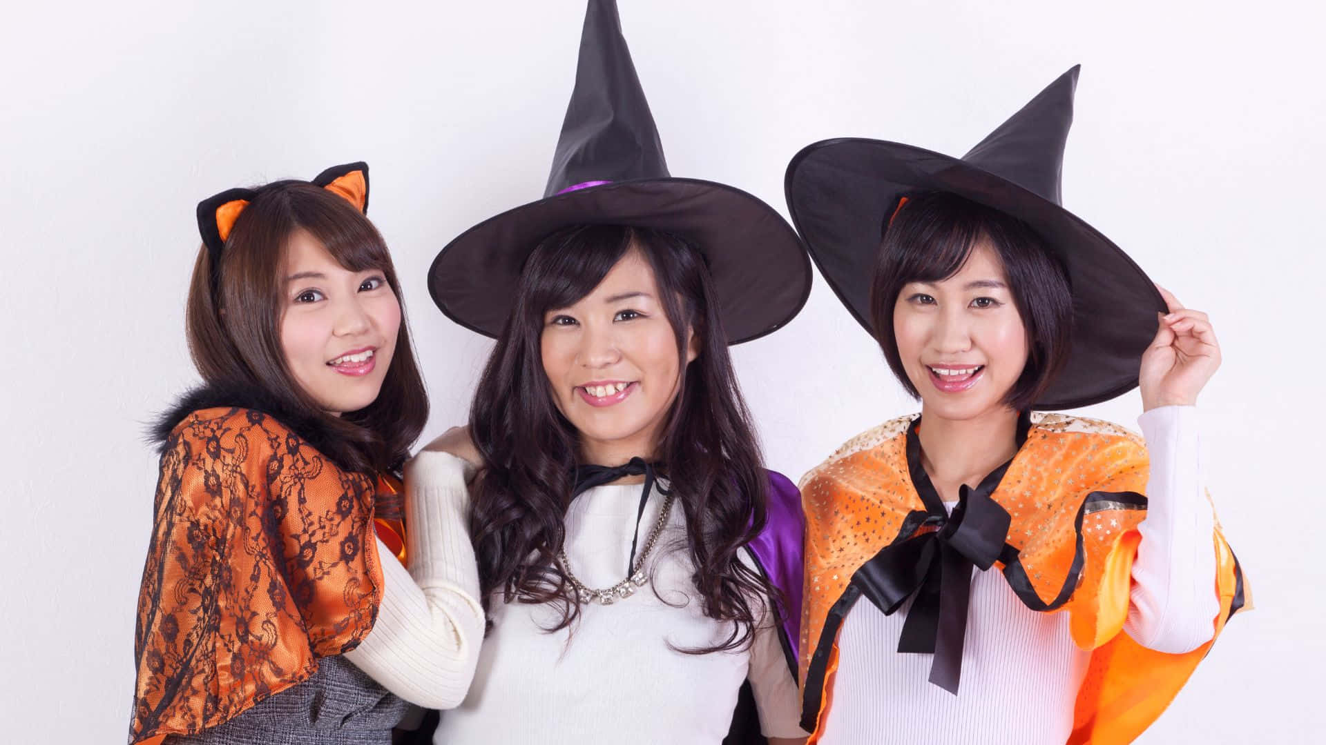 Halloween Costumes 桌布 壁紙 — 三位微笑的年輕女性穿著萬聖節服裝，在純白色背景前擺姿勢。
