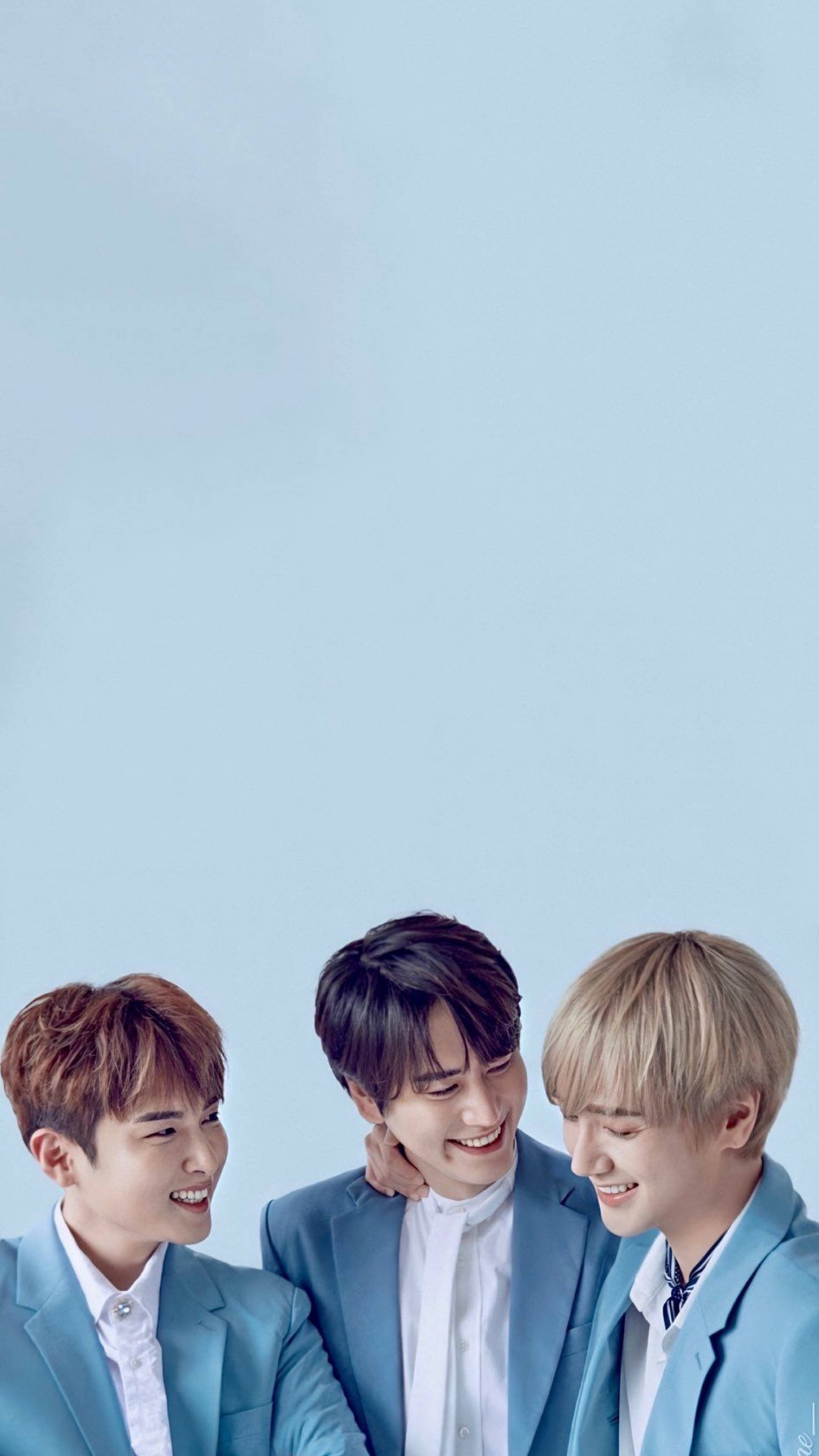 Super Junior KRY 壁紙 — 三位微笑的年輕男士穿著相配的藍色西裝，在純淺藍色背景前分享歡樂時光。