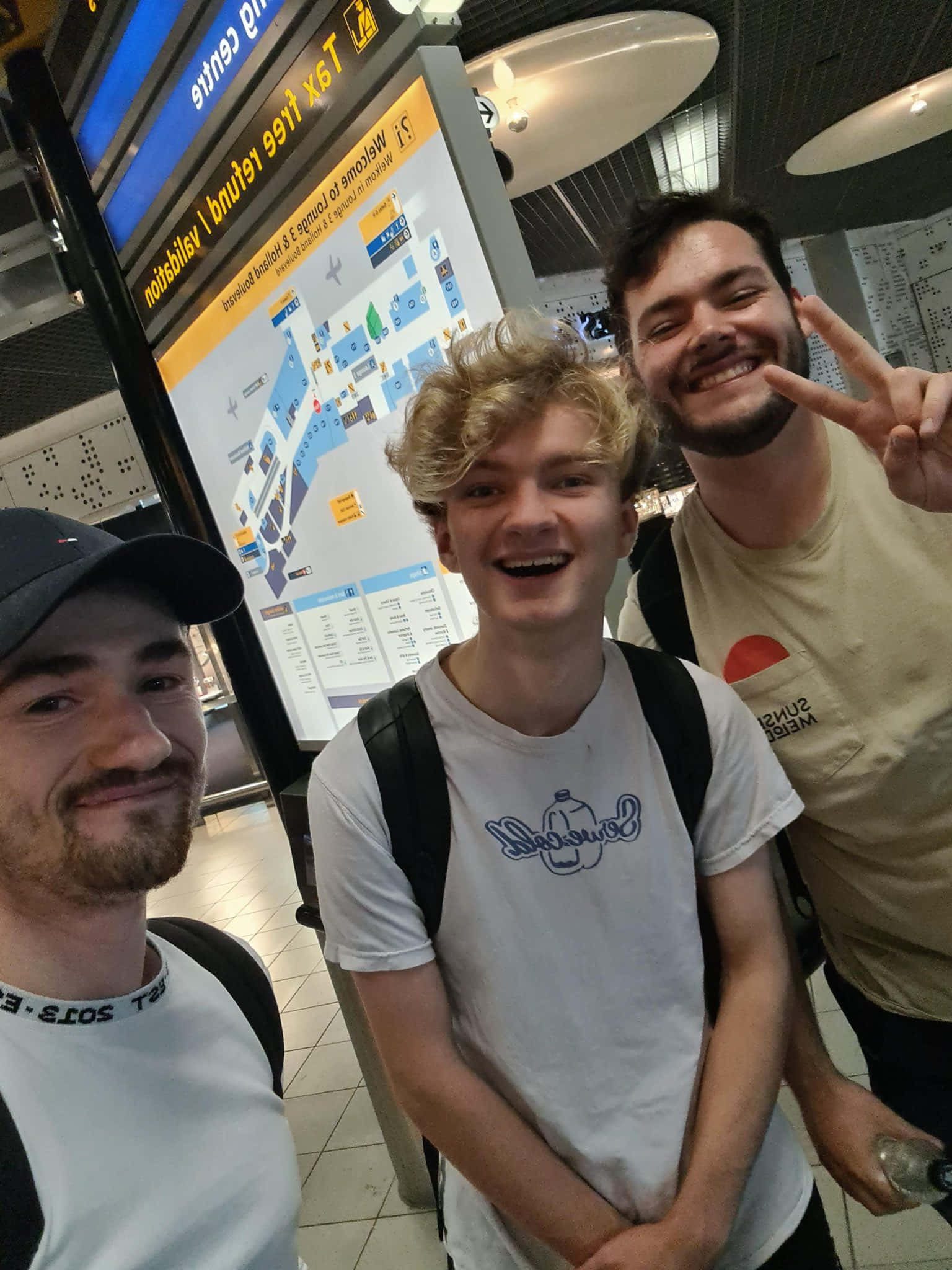 Tommyinnit 桌布 壁紙 — 三位微笑的年輕男子在機場航站樓內愉快地擺姿勢，身後有一張大地圖。